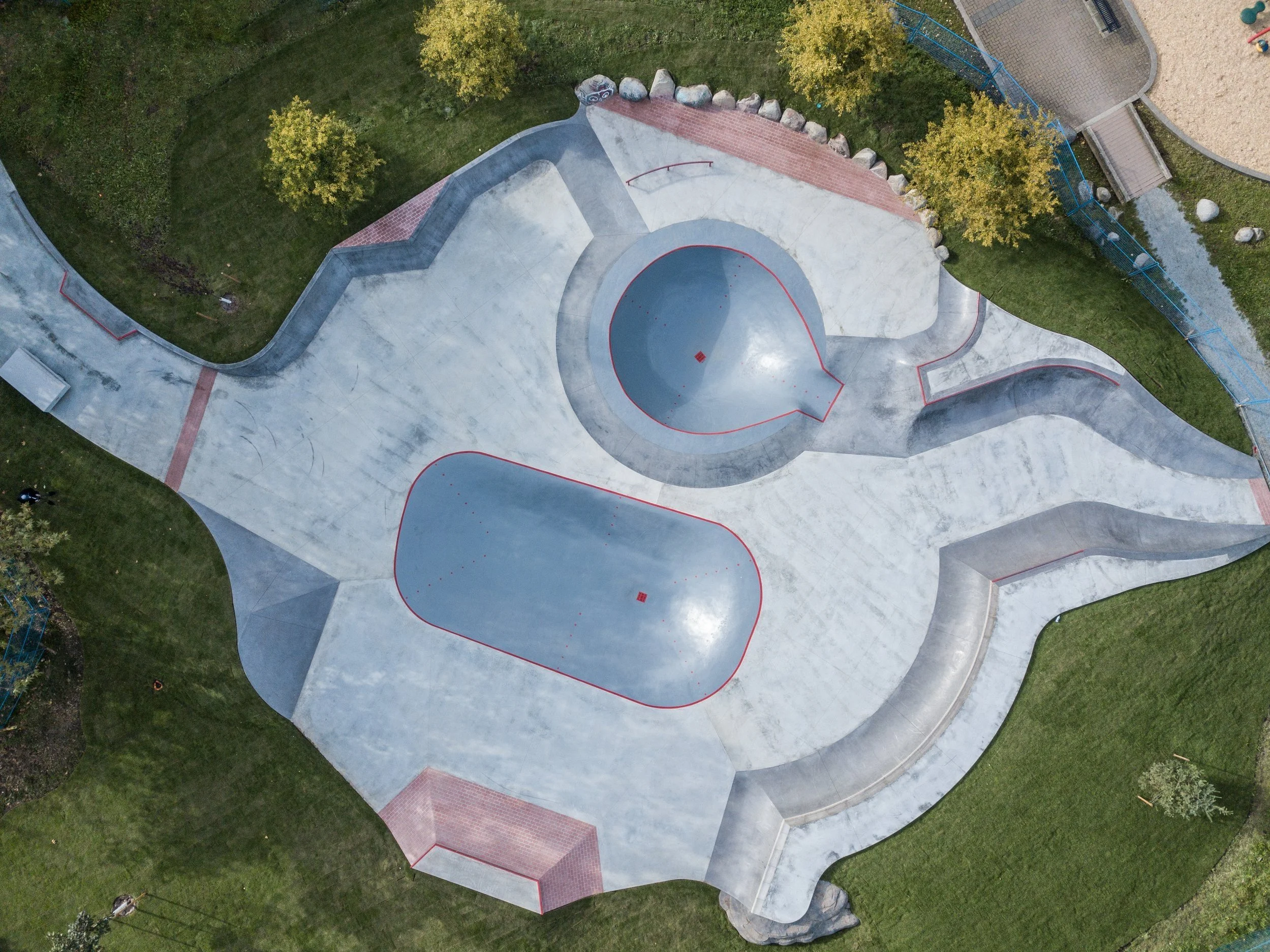 An aerial view of a skatepark with various ramps and bowls surrounded by grassy areas and trees.