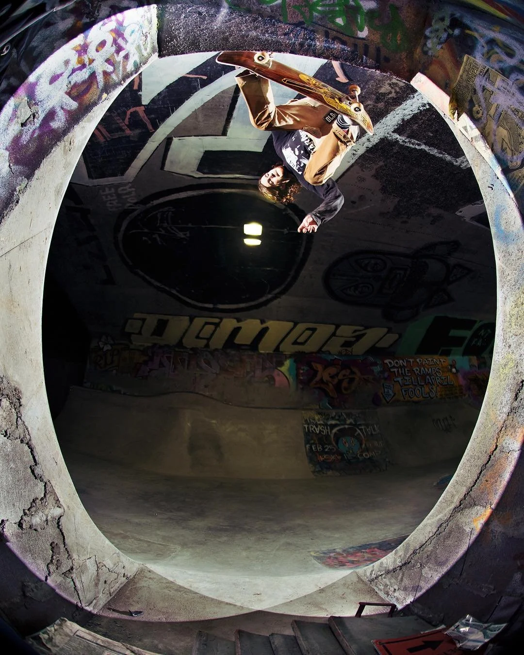 A skateboarder performing a trick inside a concrete skatepark with graffiti, seen through a fisheye lens.