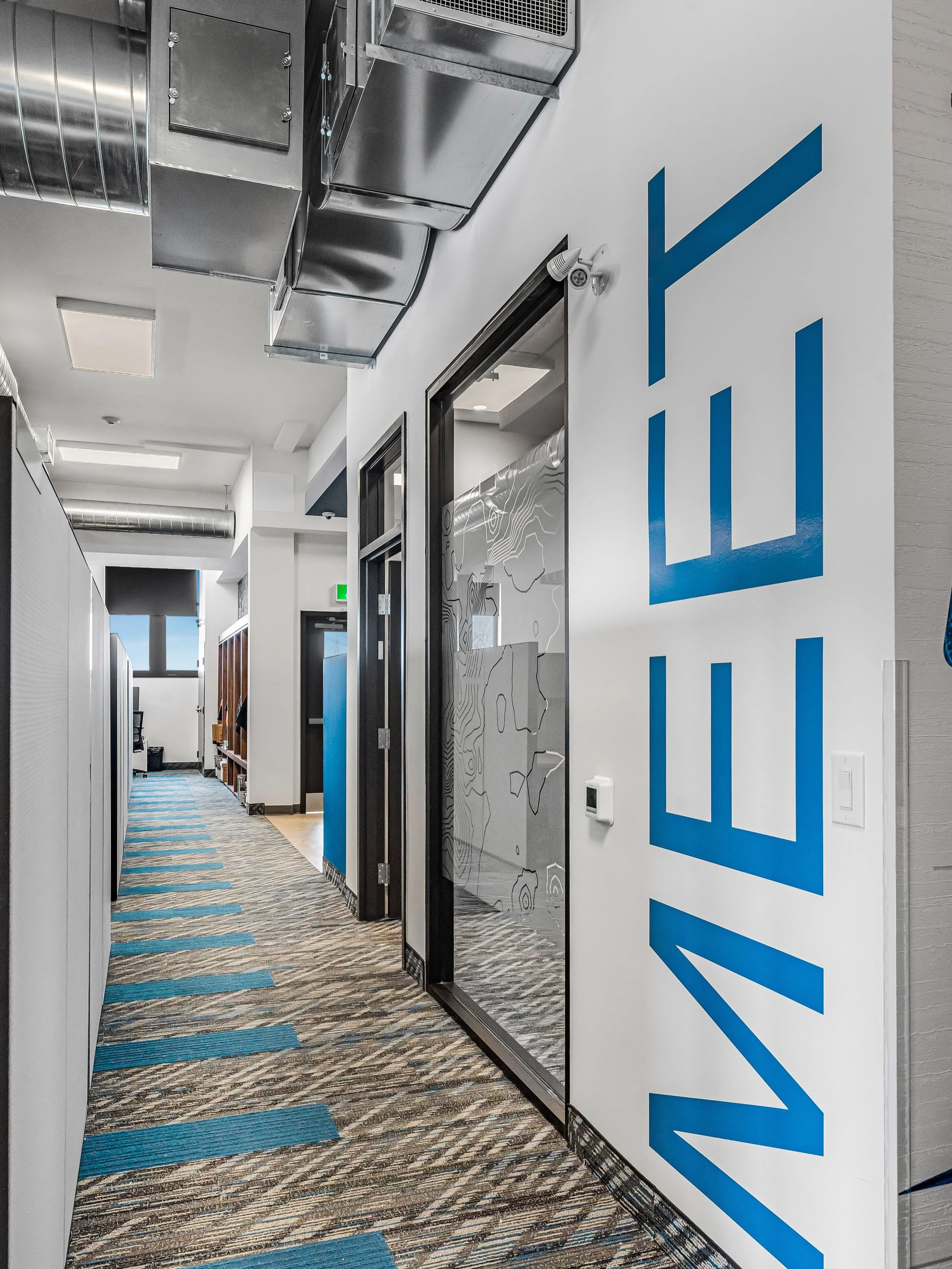 Stepping past the boardroom and into the main workflow area. Designing an open office layout is always a careful balancing act, so we integrated warm walnut acoustic ceiling baffles to cut the noise and carry the warmth throughout the office while ke
