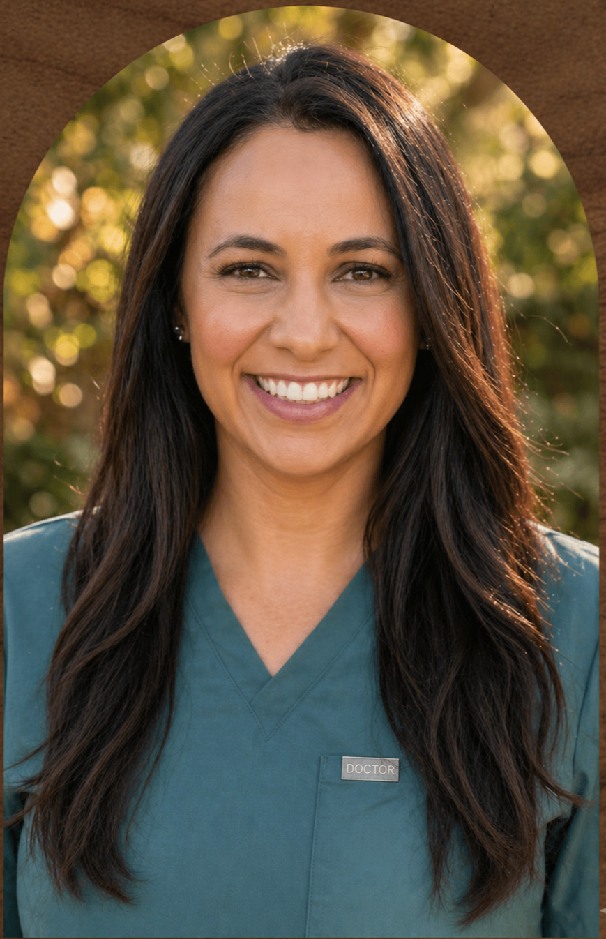Smiling woman with long dark hair wearing teal scrubs and a name tag that says "Doctor," standing outdoors with blurred trees in the background.