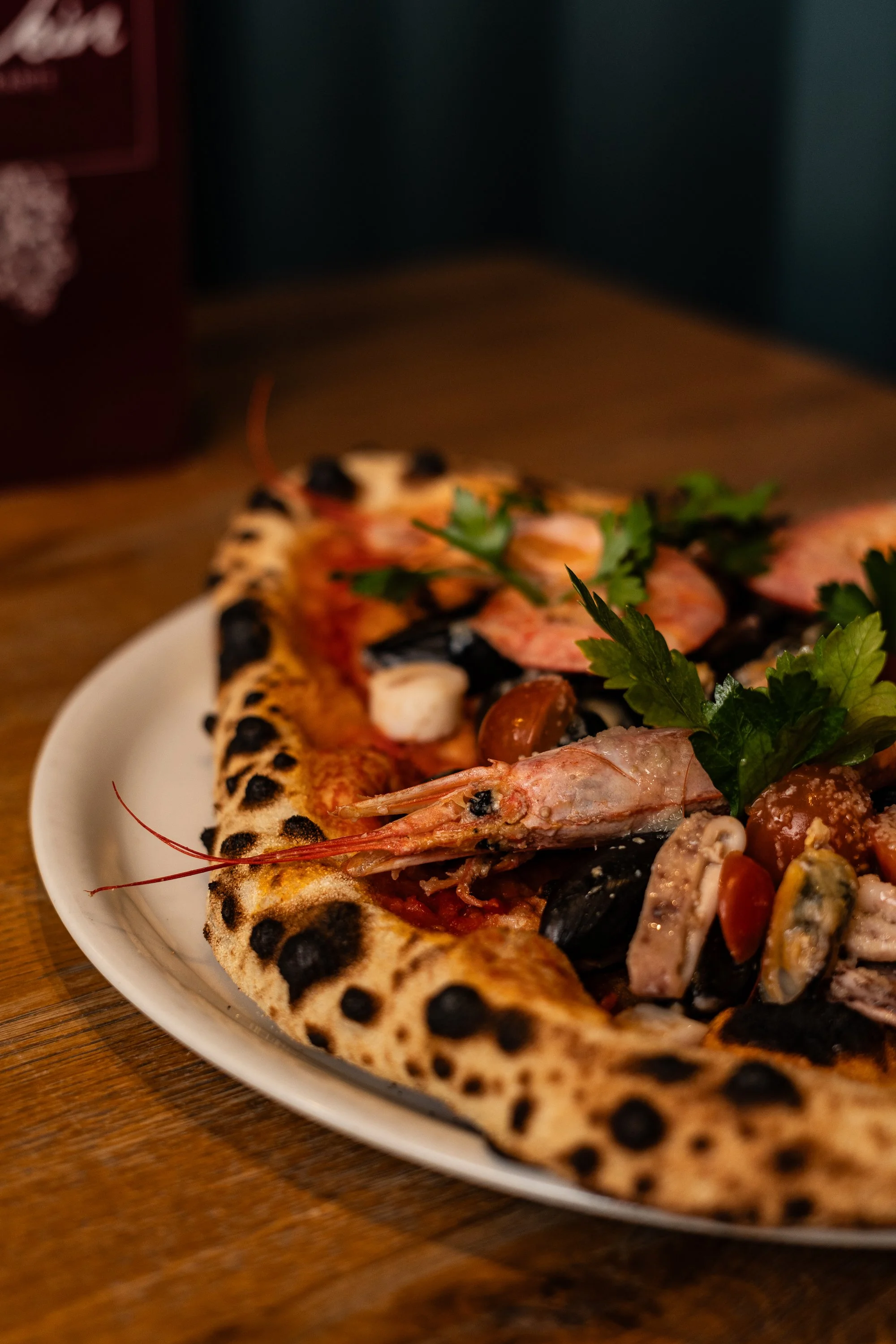 Pizza mit Meeresfrüchten, schwarzem Teig, Tomatensauce und frischer Petersilie.