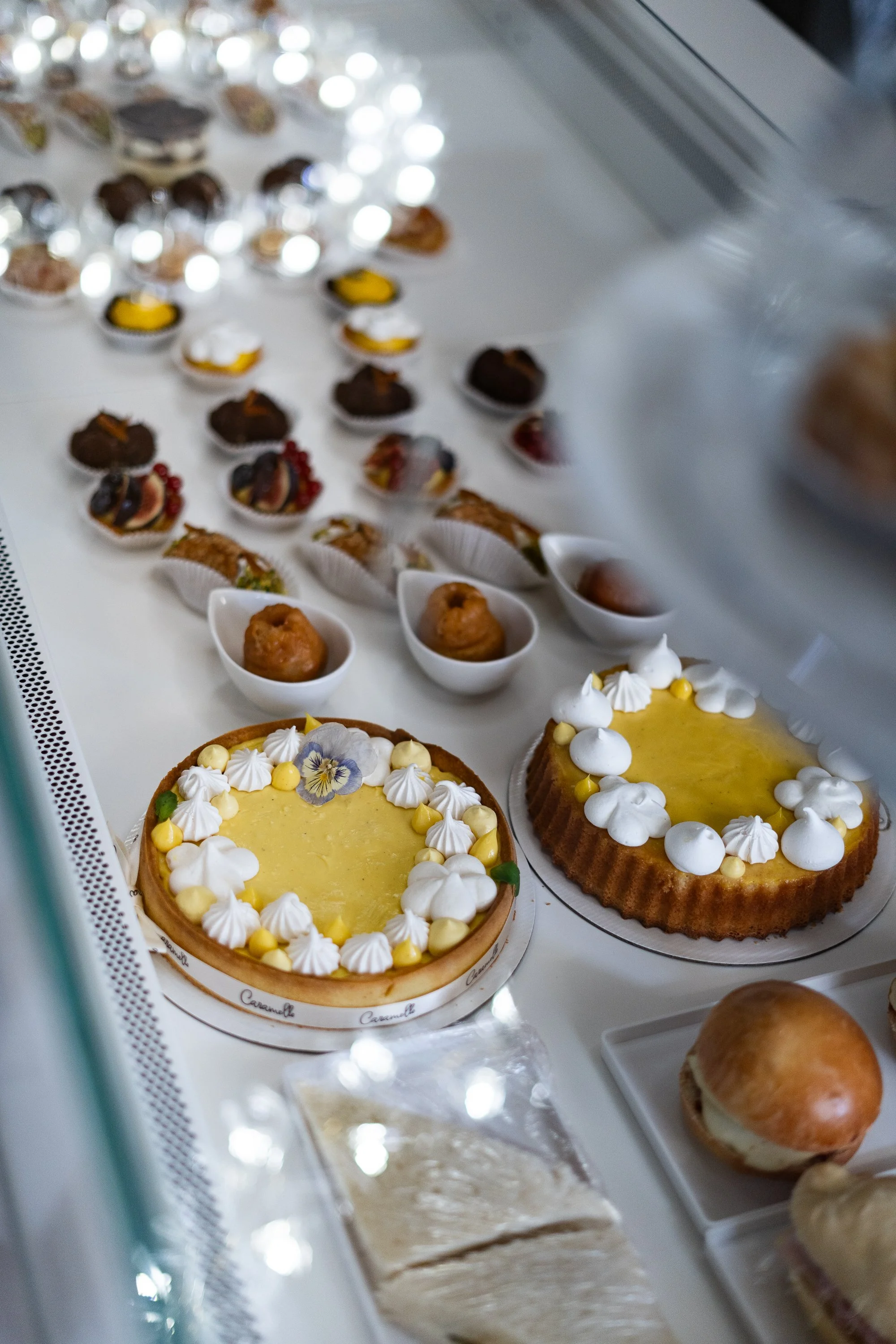 Verschiedene Torten und Desserts in einer Konditorei-Auslage, darunter Zitronentörtchen, kleine Kekse, Frucht- und Schokoladendecken sowie Pasteten