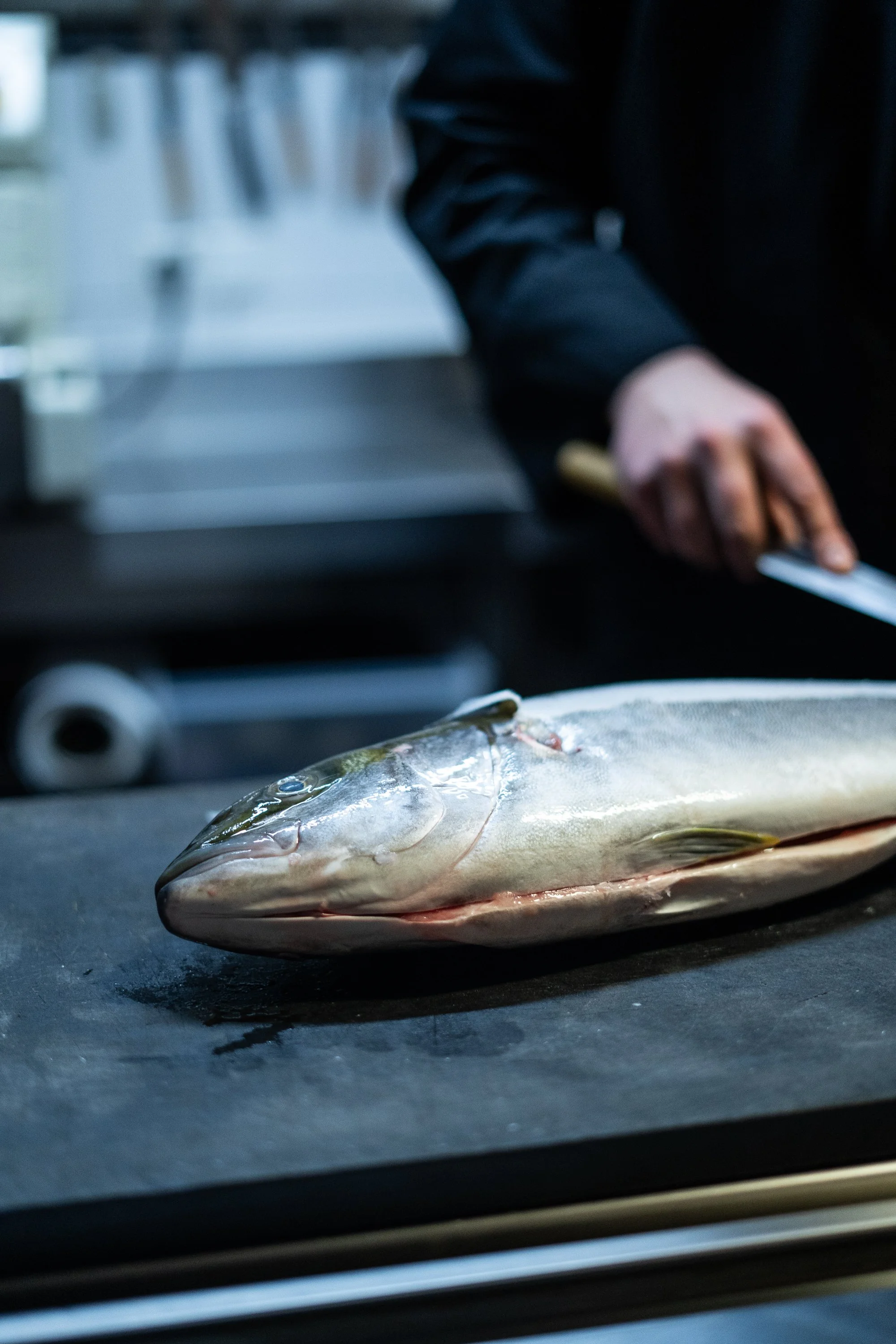 Frischer Heilbutt liegt auf einer Arbeitsfläche, ein Messer ist im Hintergrund in der Hand einer Person, die bereit ist, den Fisch zu zubereiten.