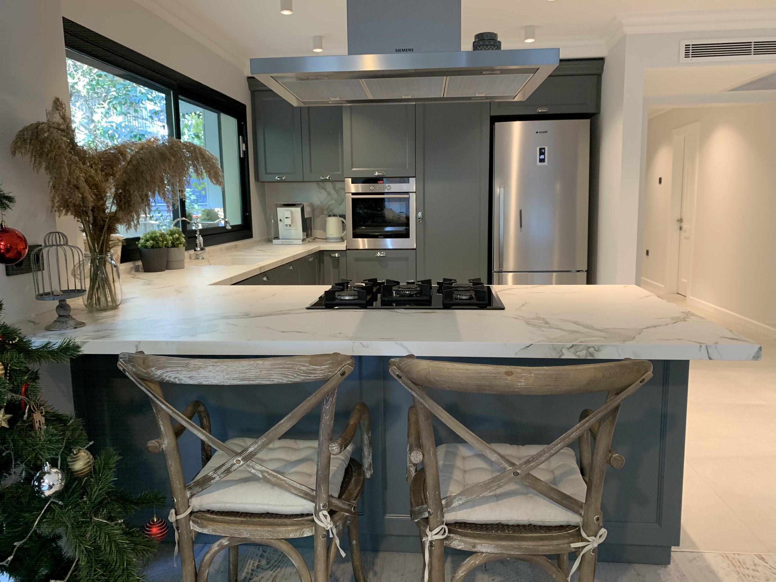 Close up view from the kitchen counter of a luxurious modern kitchen boasting quartz countertops, custom serene hunter forest green cabinetry, and high-end stainless steel appliances.