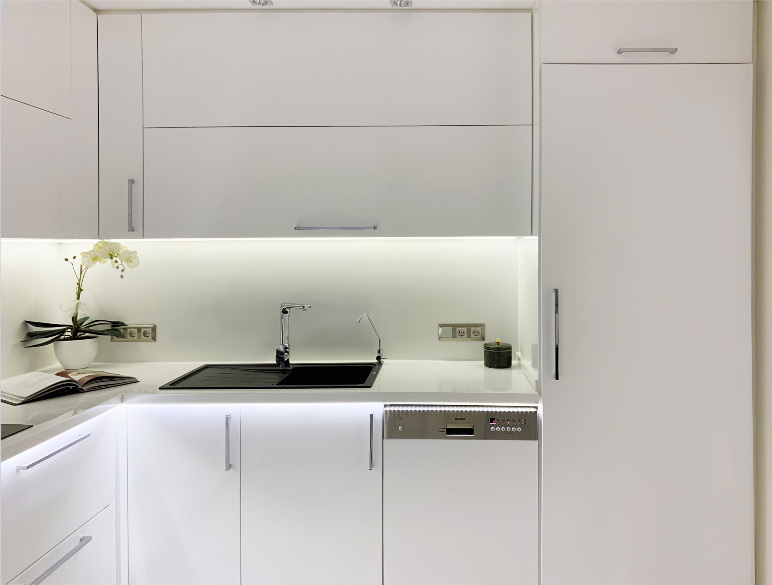 A modern kitchen with grey quartz countertops, white cabinetry, under cabinet lighting, and high-end stainless steel appliances.