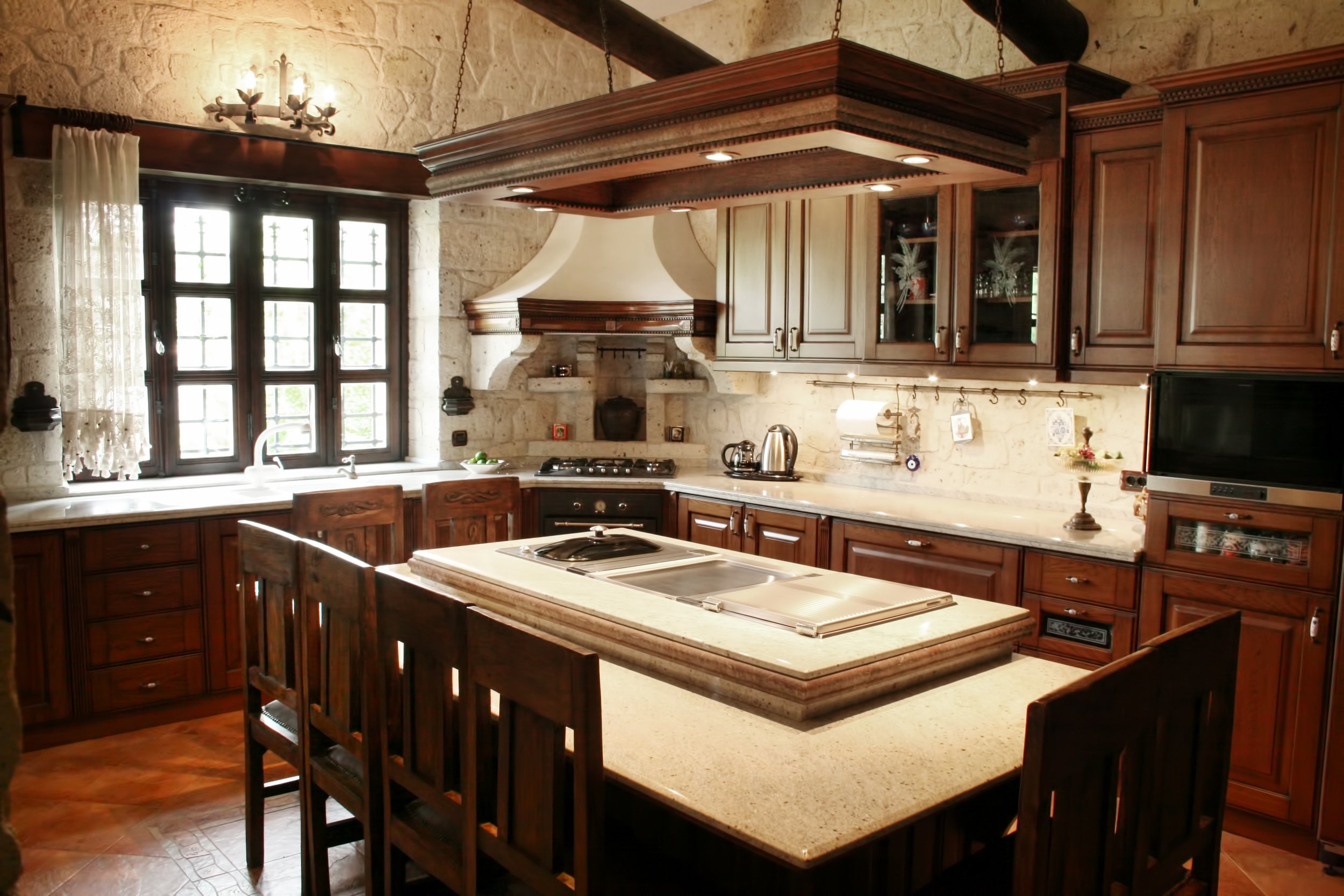 A cozy kitchen with a central island and rustic dark walnut wooden cabinets, a farmhouse sink, and vintage-style custom made lighting fixtures.