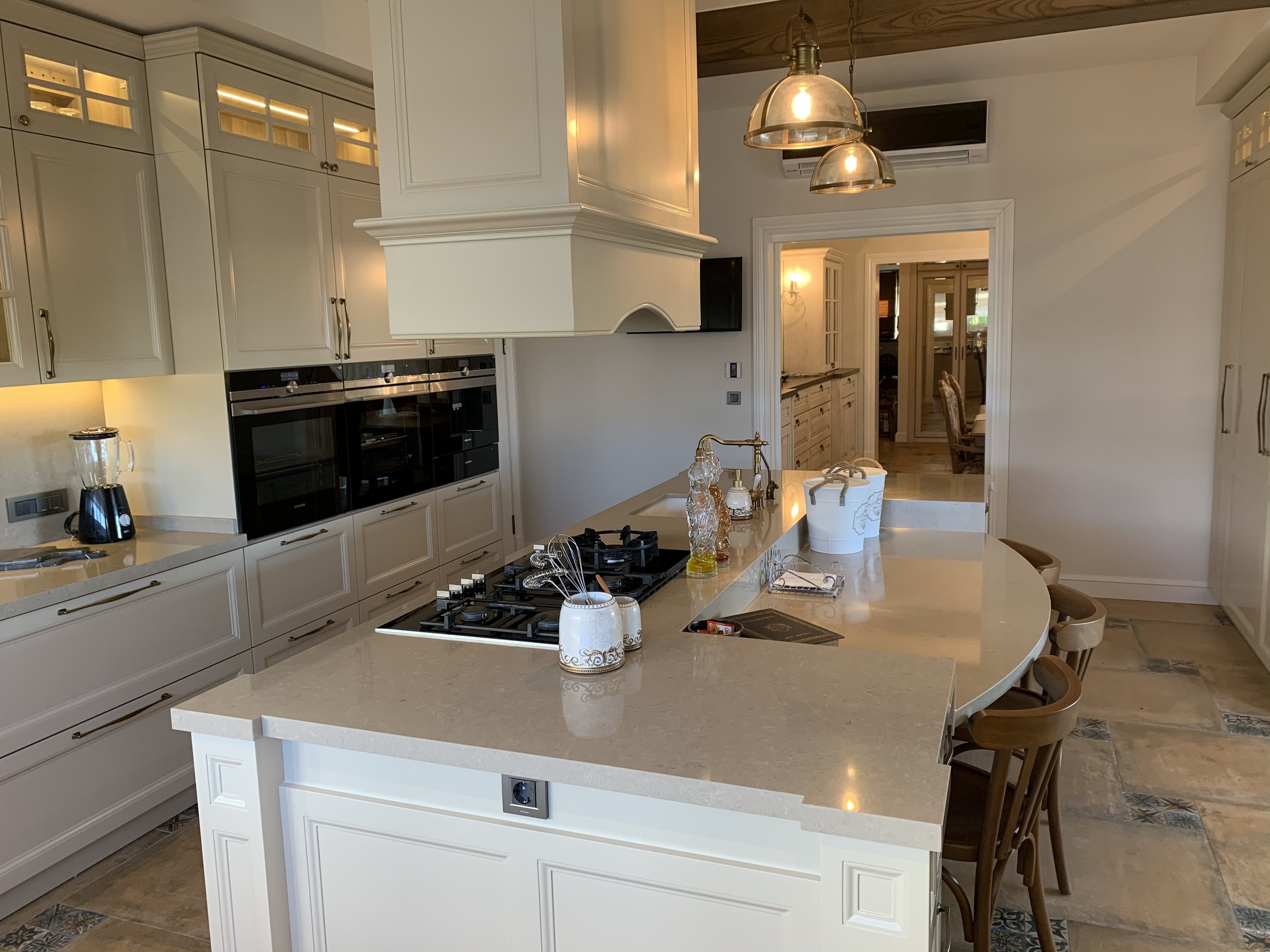 A large luxury modern rustic kitchen with a central island, beige wooden cabinets, beige quartz countertops, and vintage-style custom made accessories.