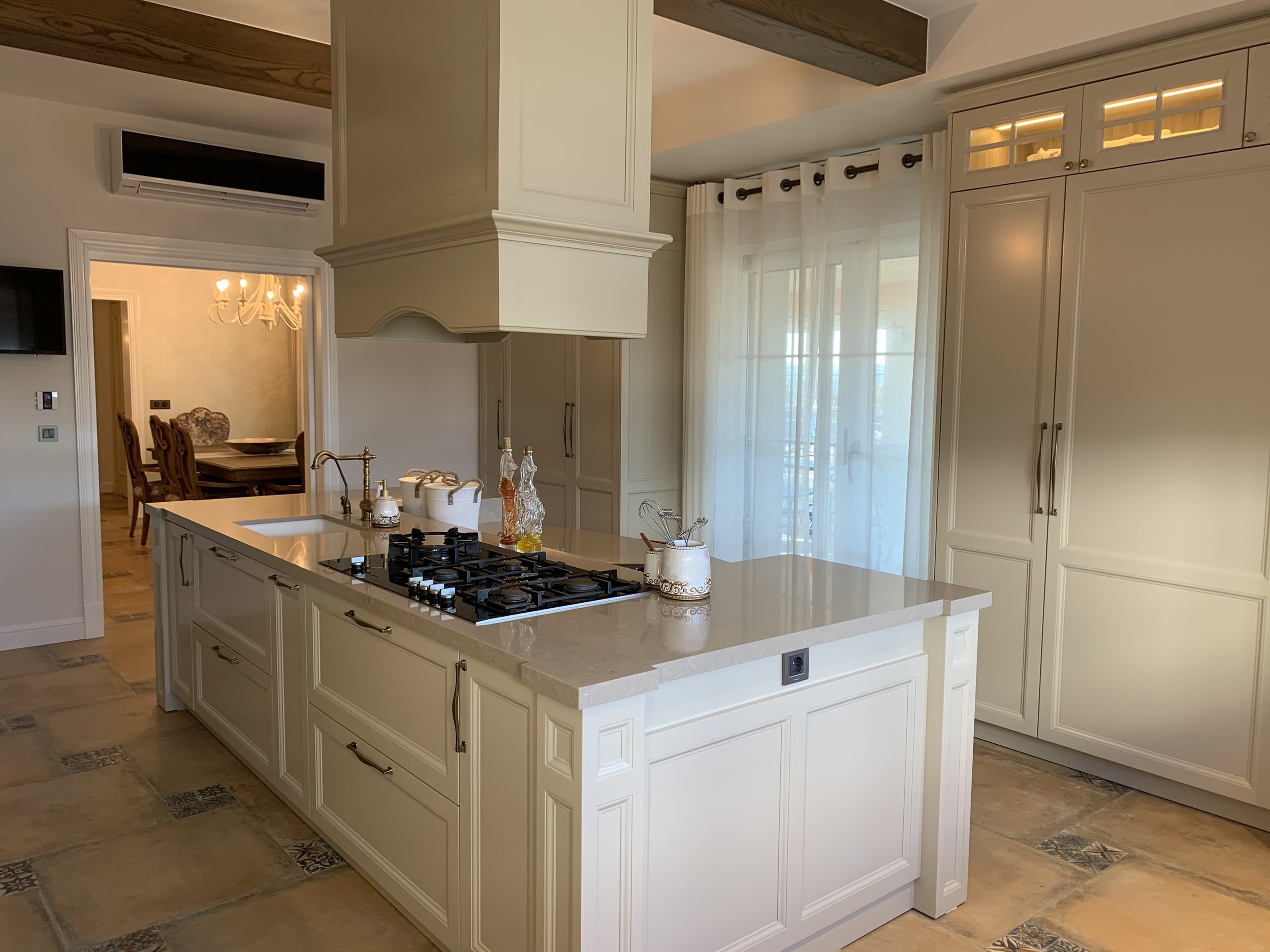 A large luxury modern rustic kitchen with a central island, beige wooden cabinets, beige quartz countertops, and vintage-style custom made accessories.