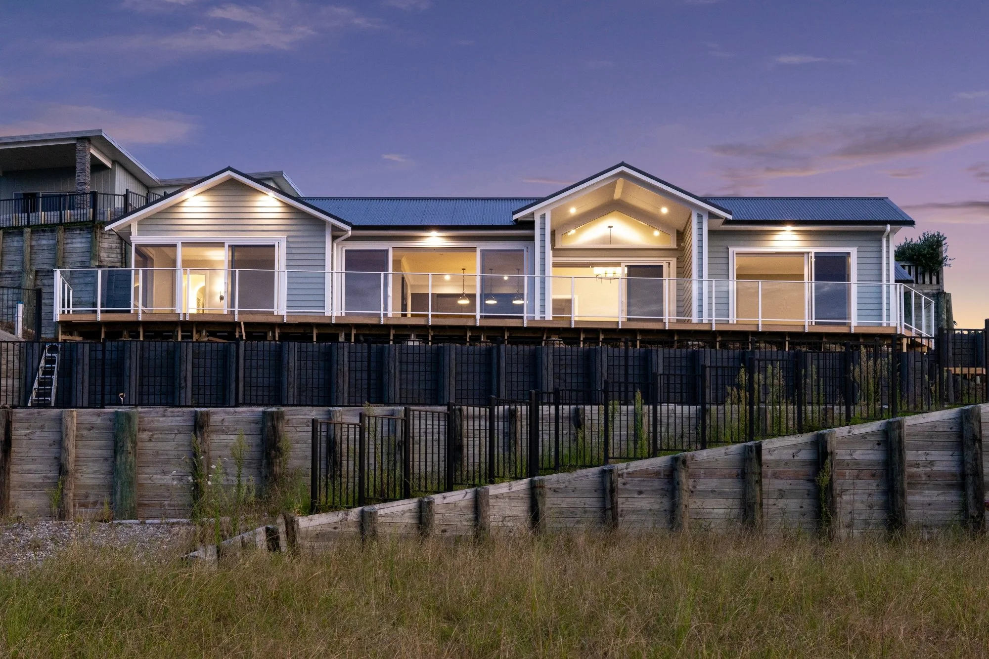 Modern house with elevated deck and large windows, illuminated at twilight.
