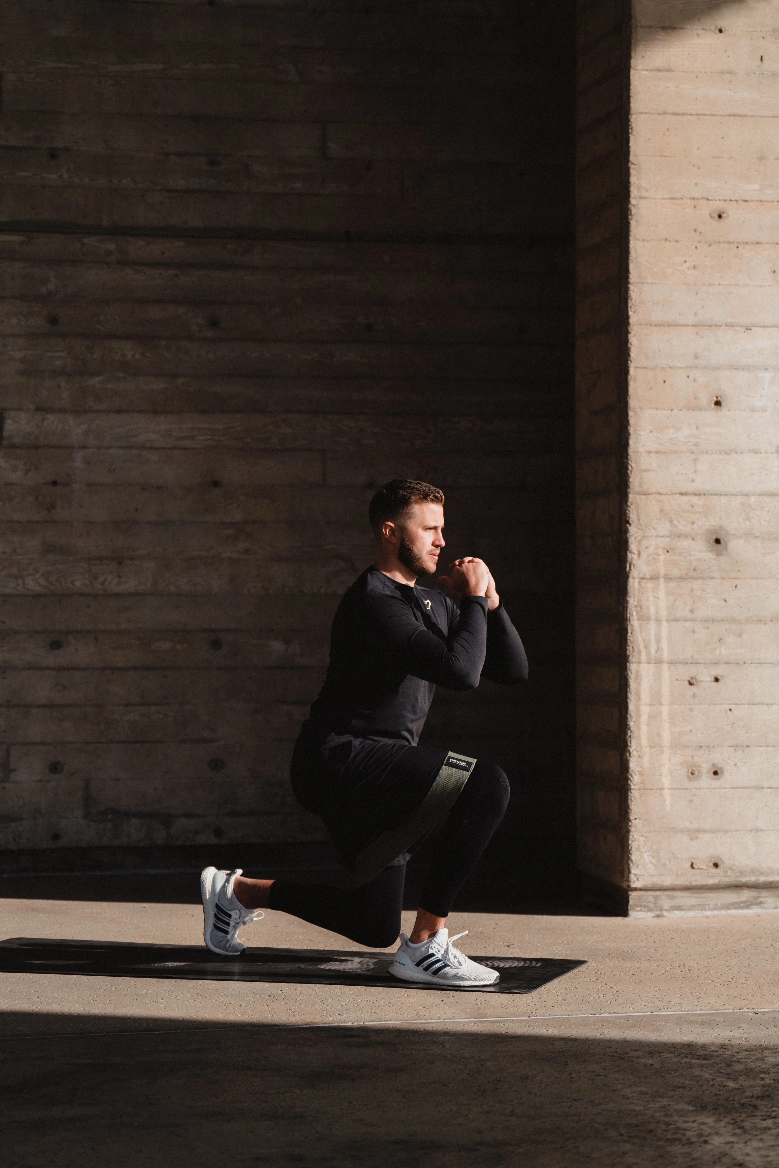A man doing a squat exercise on a black yoga mat in an outdoor industrial setting.