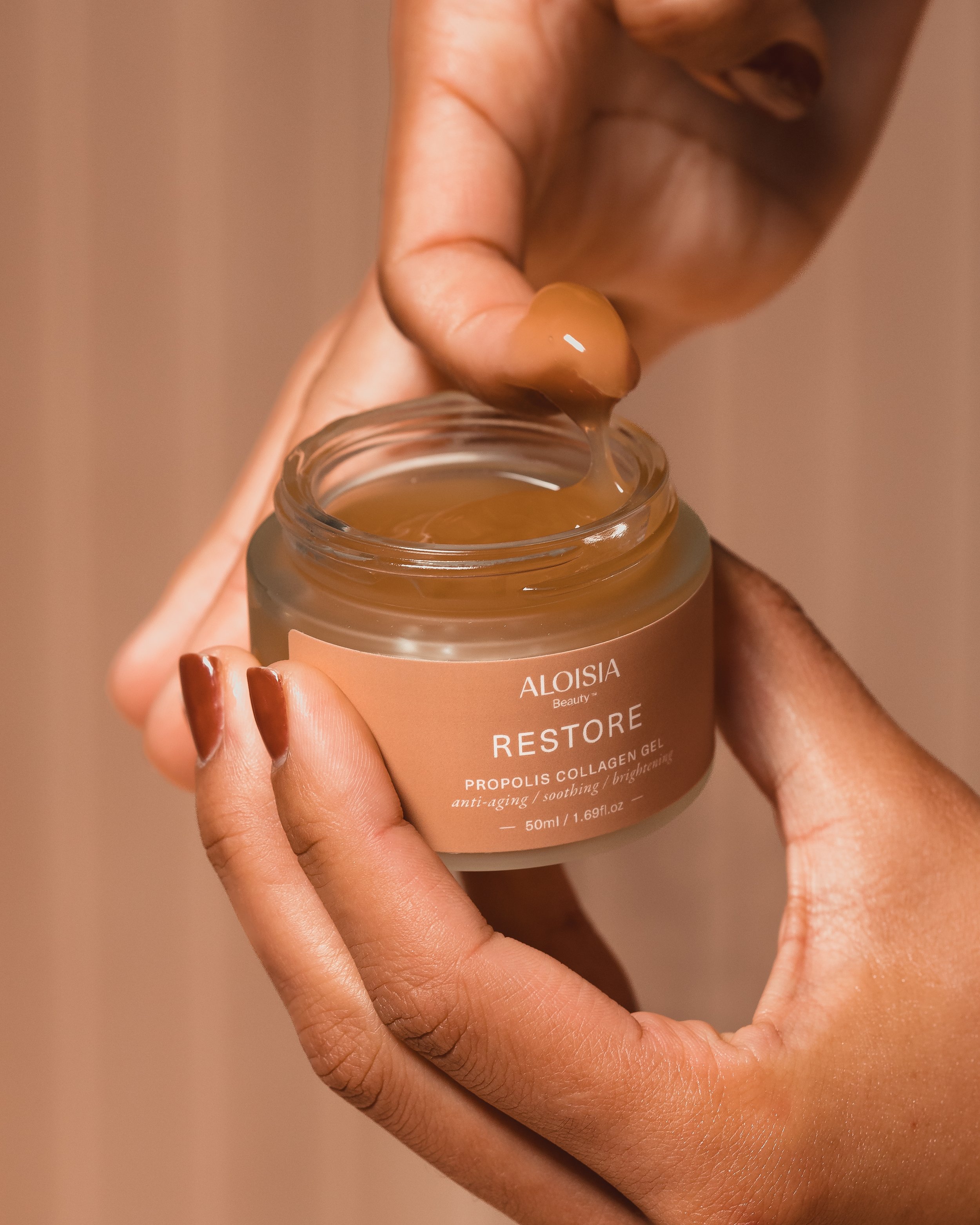 A hand holding a jar of Aloisia Beauty Restore Propolis Collagen Gel, with some gel on the finger.