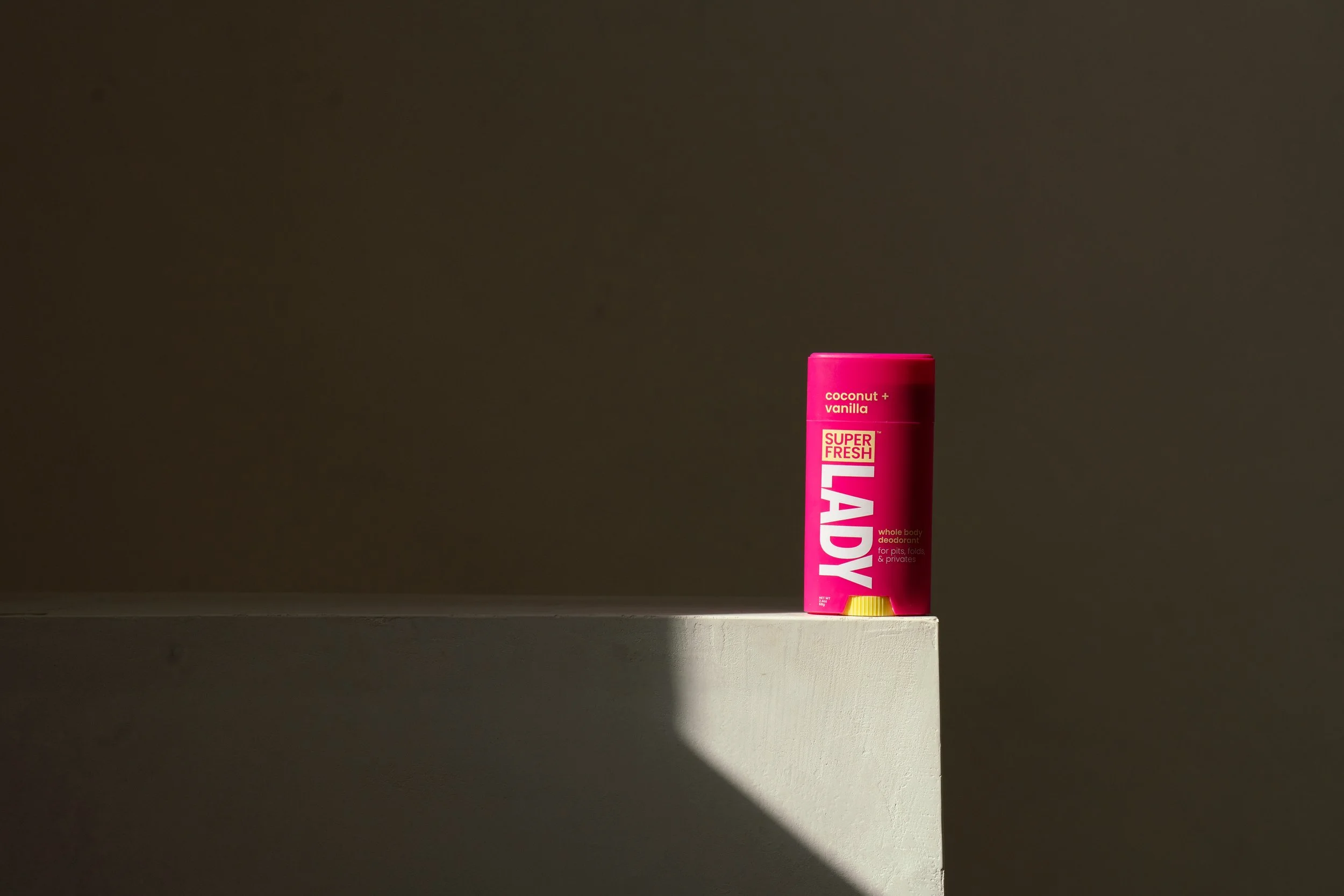 A pink container of Lady deodorant labeled 'Super Fresh Coconut + Vanilla' on a white shelf with shadowed background.