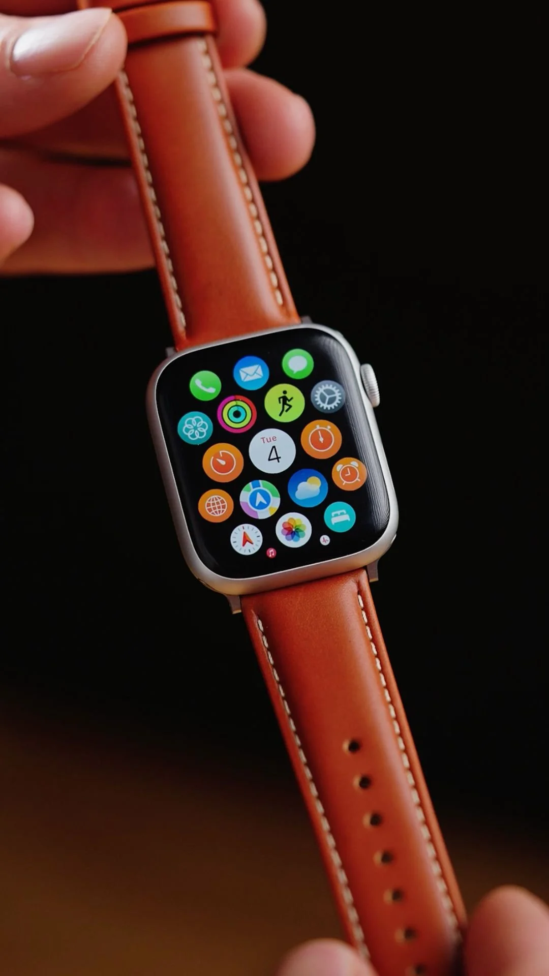 Apple Watch with a brown leather band displaying a colorful app grid on a black background.