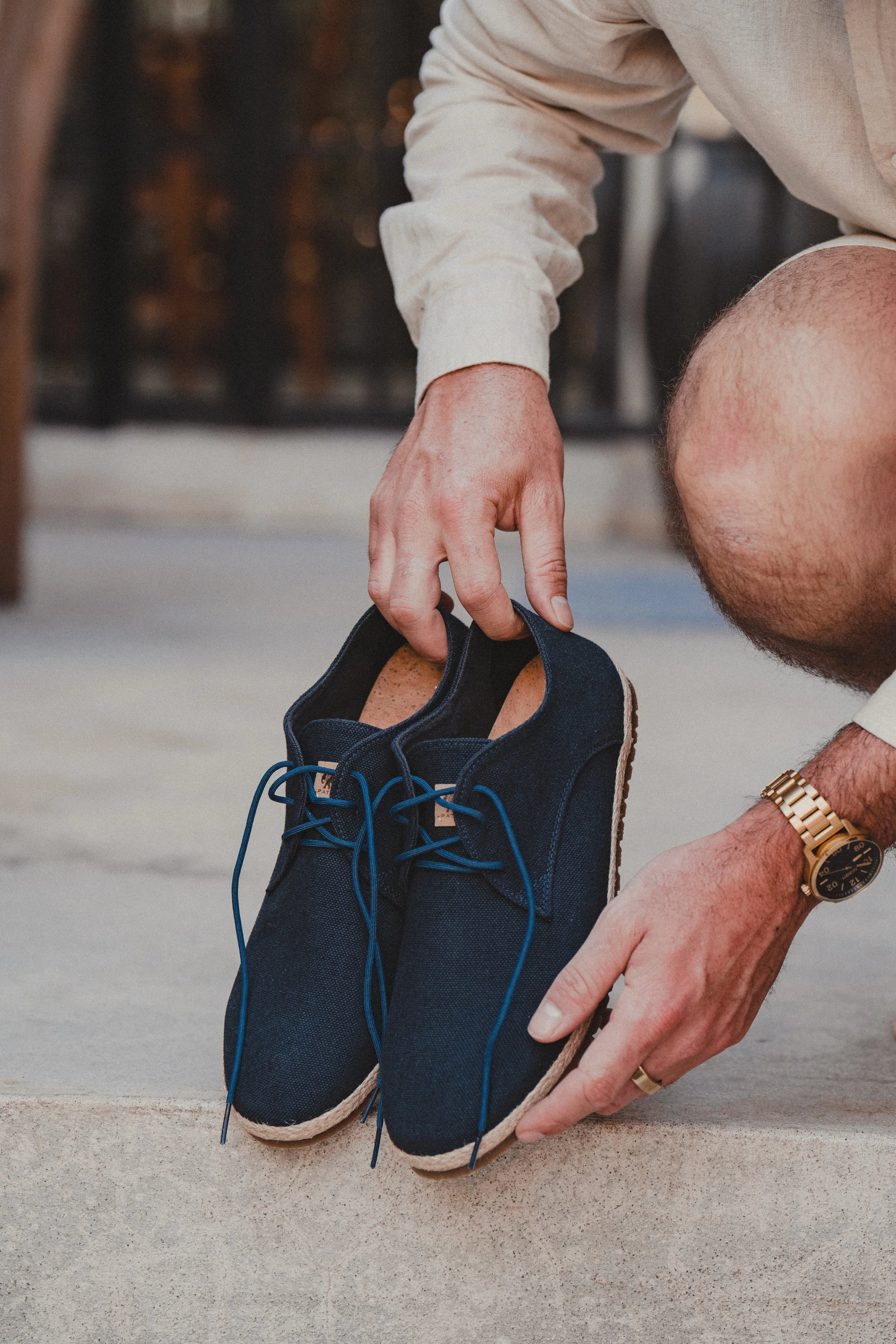 Person kneeling outdoors placing navy blue canvas shoes on a concrete surface.