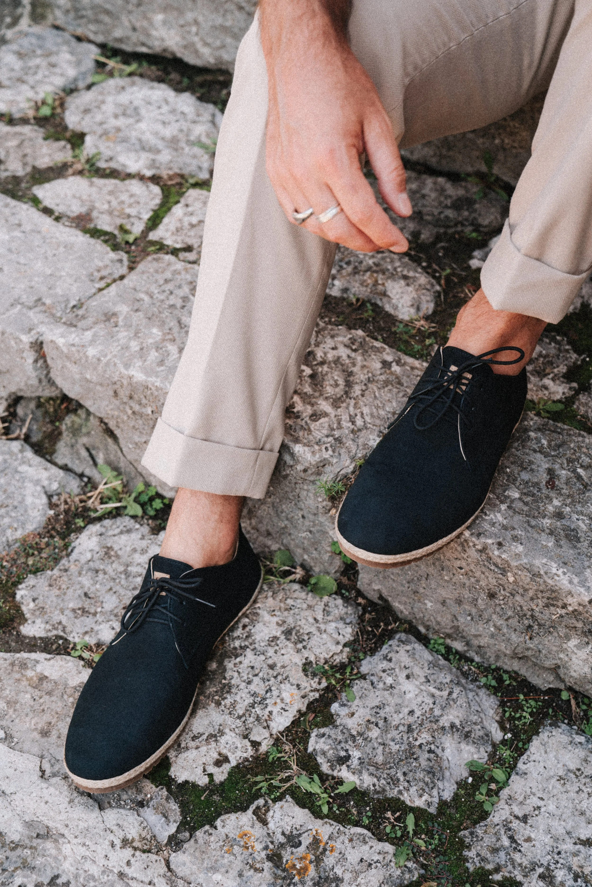 A person wearing beige pants and black shoes sitting on a cobblestone ground.