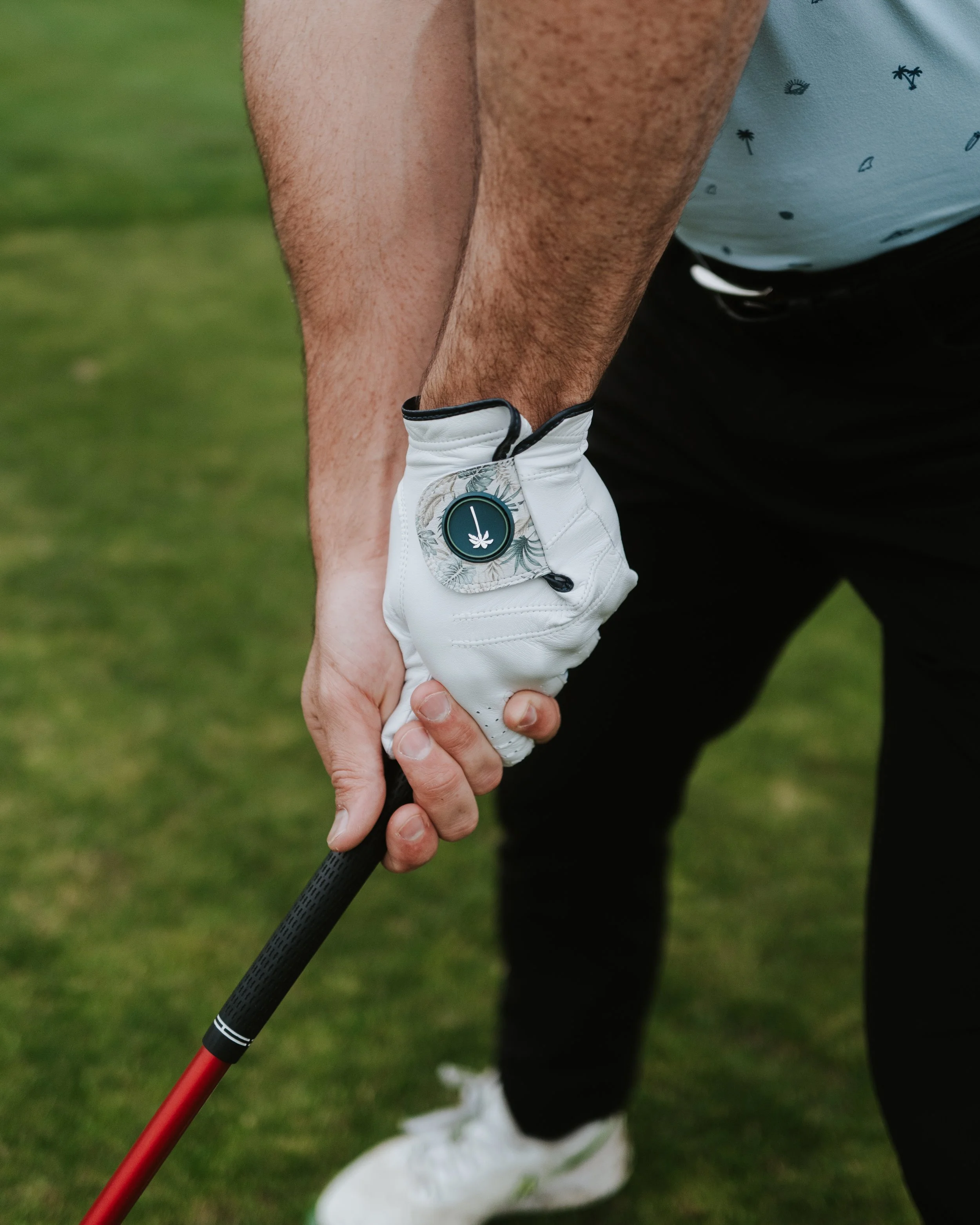 Close-up of a person with a white golf glove holding a golf club, standing on a grassy golf course.