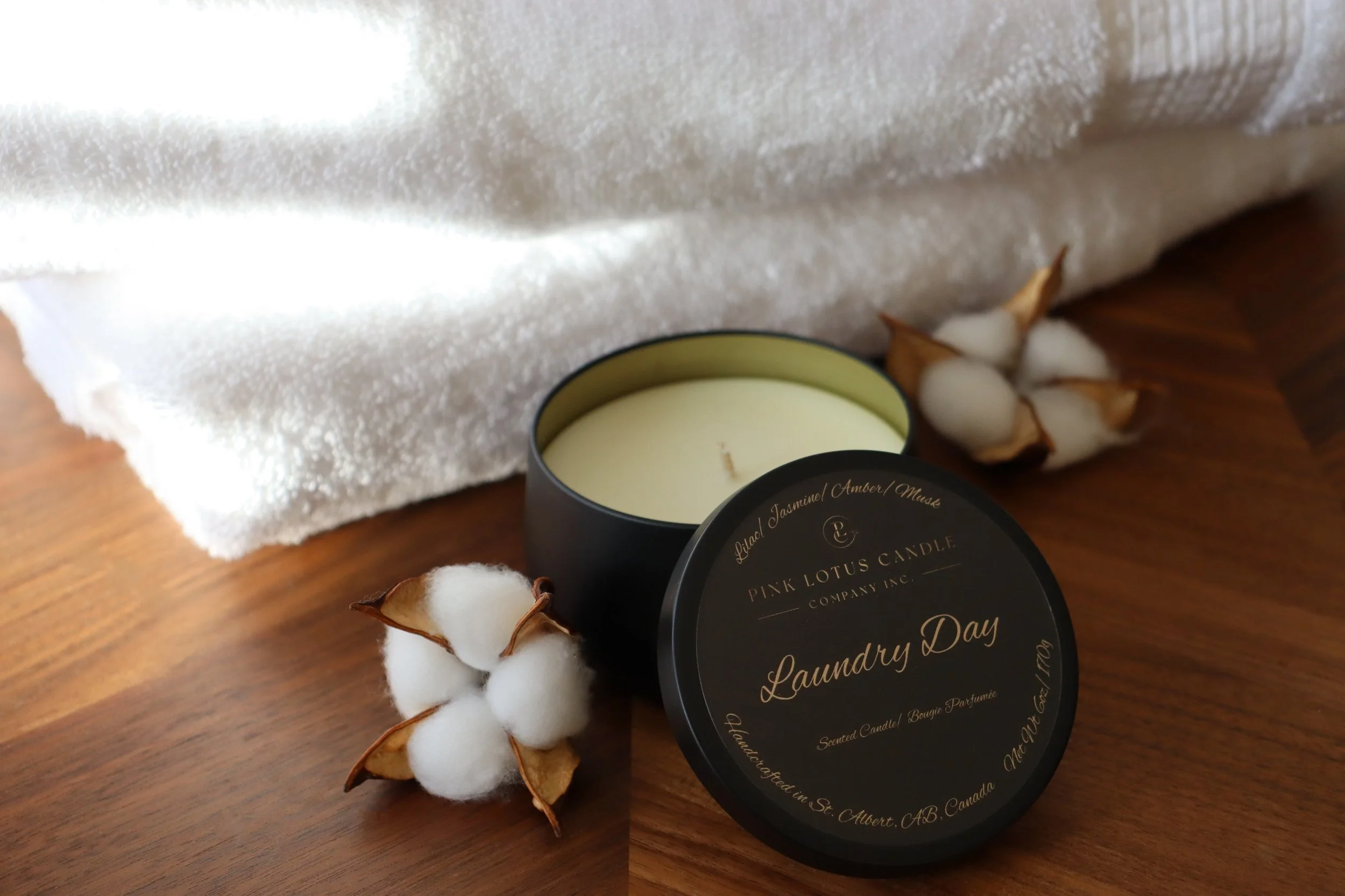 A Laundry Day scented black candle tin next to folded towels and cotton pods