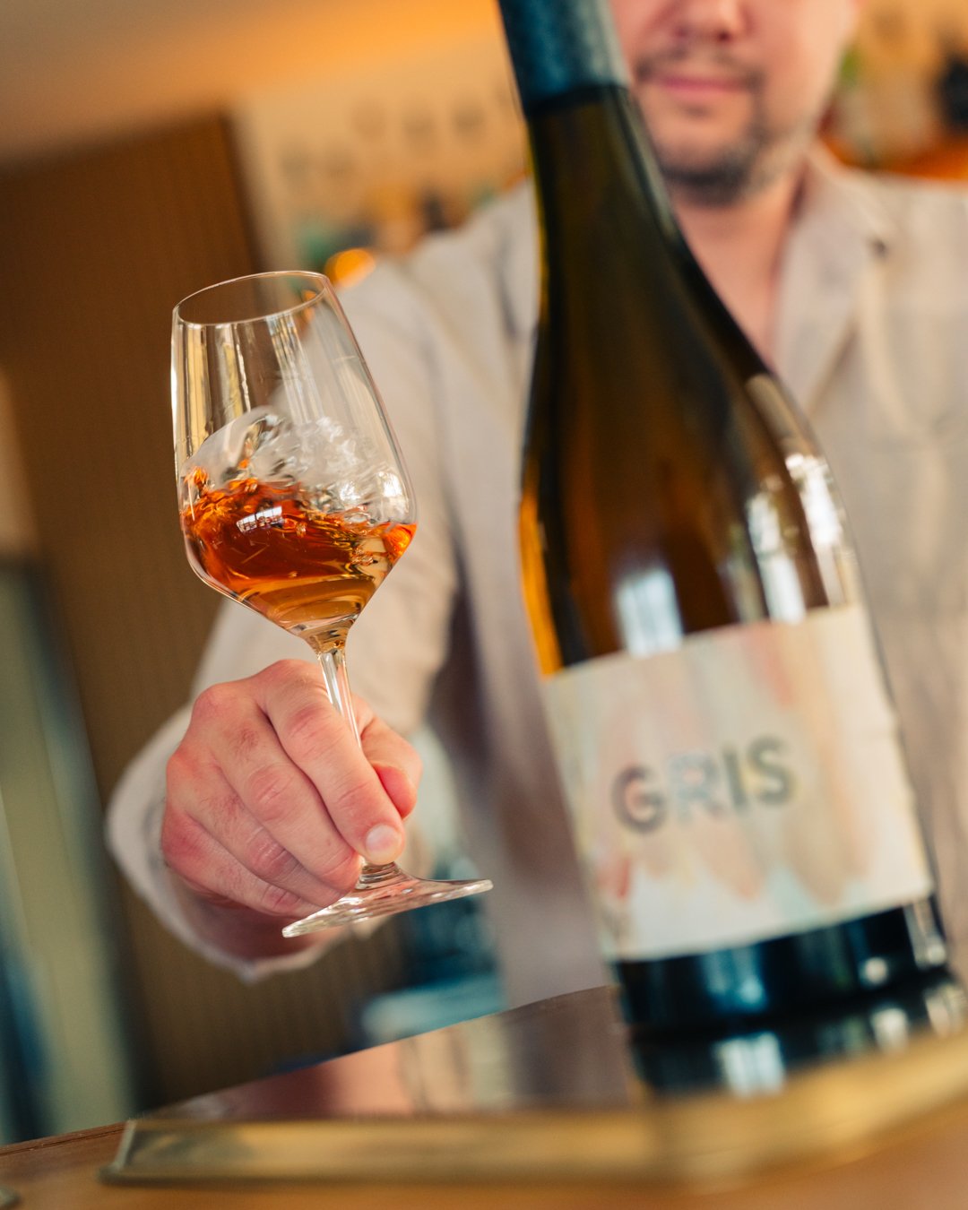 A person holding a glass of Mulline Pinot Gris with the bottle, labeled 'GRIS' in the foreground.