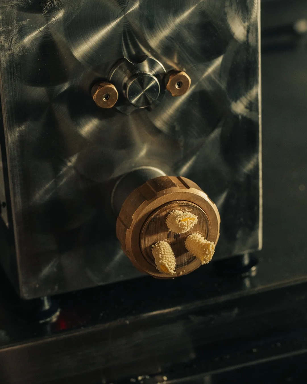 Close-up of a pasta extruder with a brassnrotary knob and small white, textured objects attached to the front.