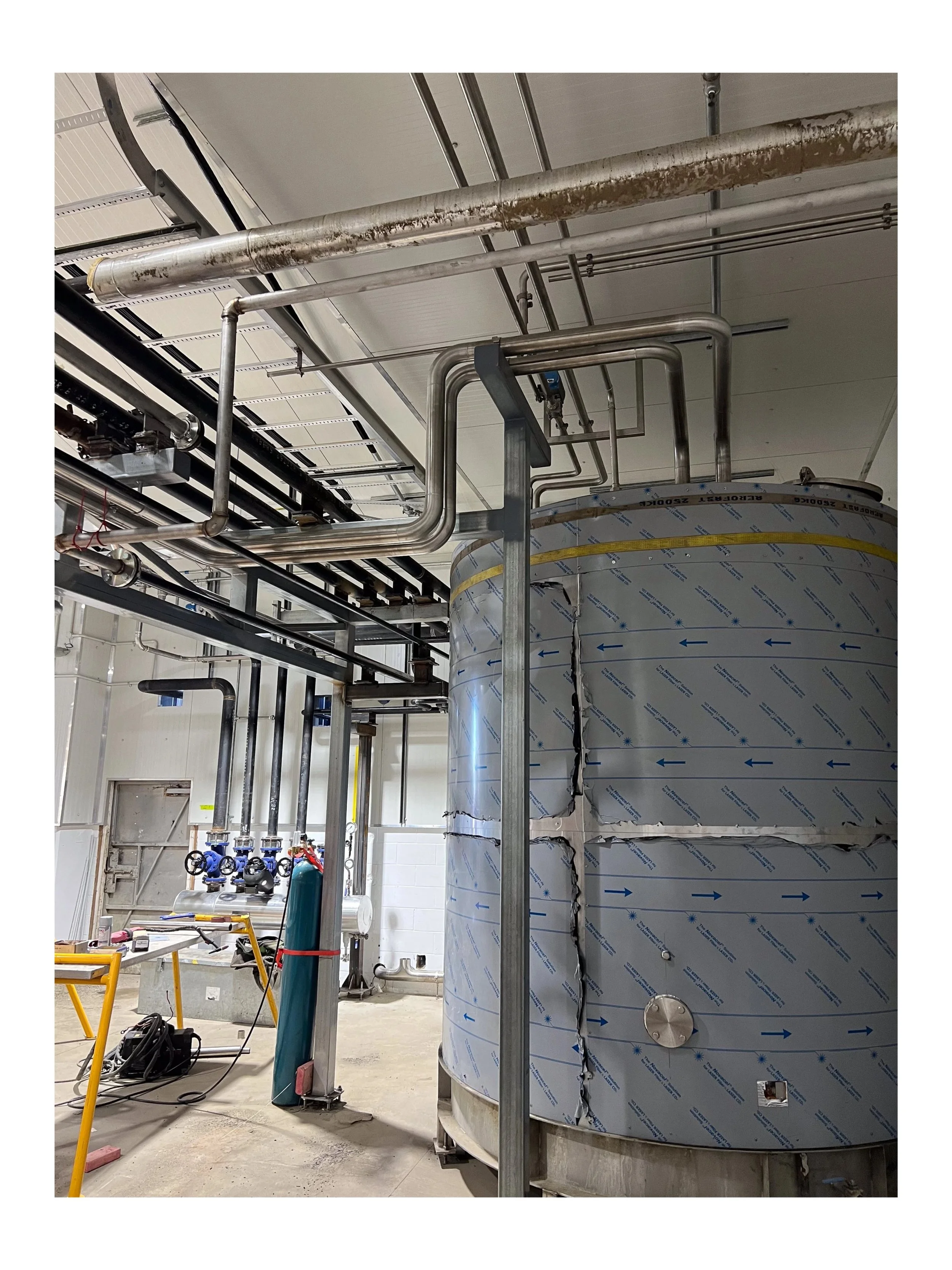 Industrial stainless steel tank with piping system in a manufacturing facility.