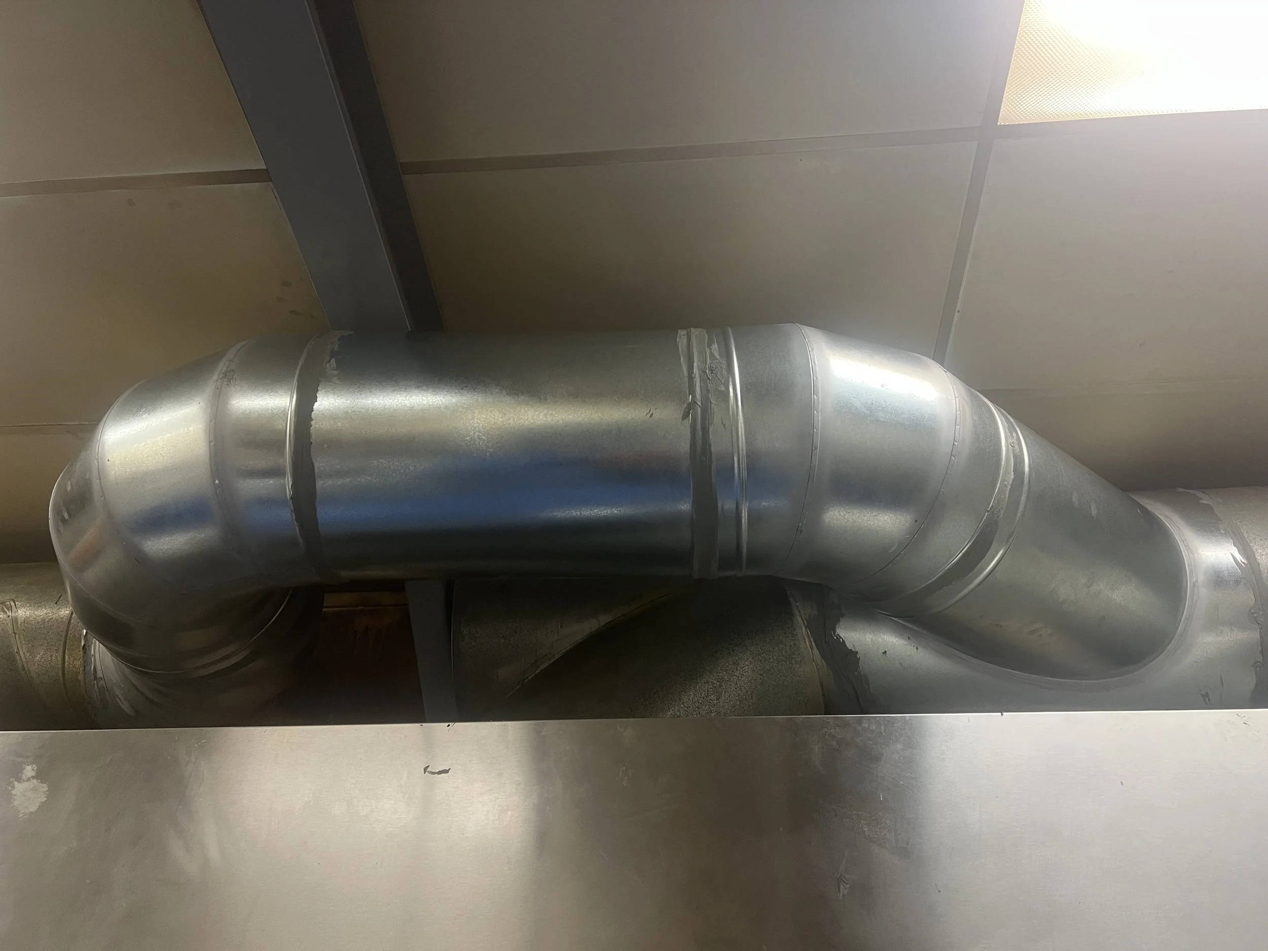 Metal ventilation duct with a bend, attached to a ceiling.
