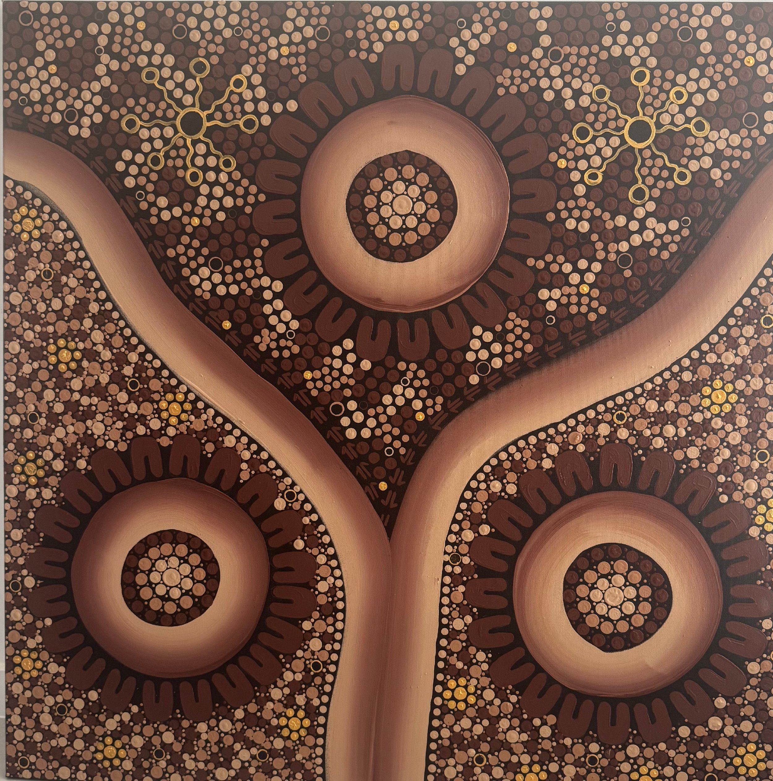 Aboriginal dot painting with circular and dotted patterns in earth tones of brown, beige, and gold, featuring three large circular motifs connected by curved bands.