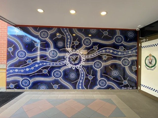 A large mural with a dark blue background featuring abstract, interconnected white and yellow circular patterns and lines, with a central clock showing the time.