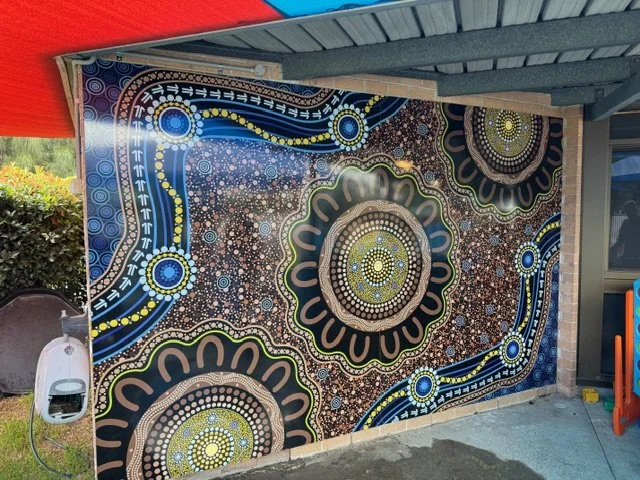 Colorful abstract mural with intricate circular and swirling patterns in blue, yellow, black, and white on a wall.