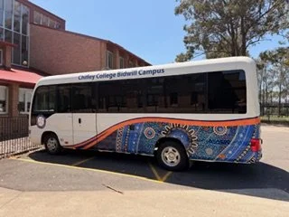 A white bus with decorative blue and orange patterns parked on a street near a building and trees.