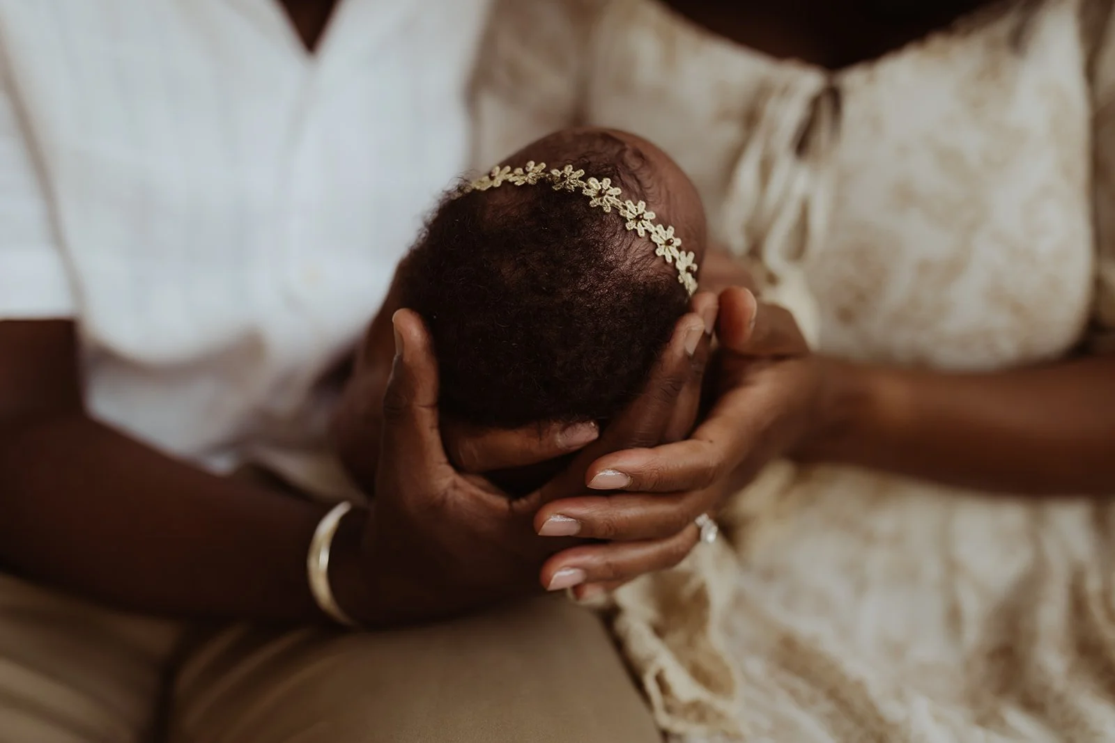 A mom and dad hold their baby girl in their hands and admire her beautiful hair.