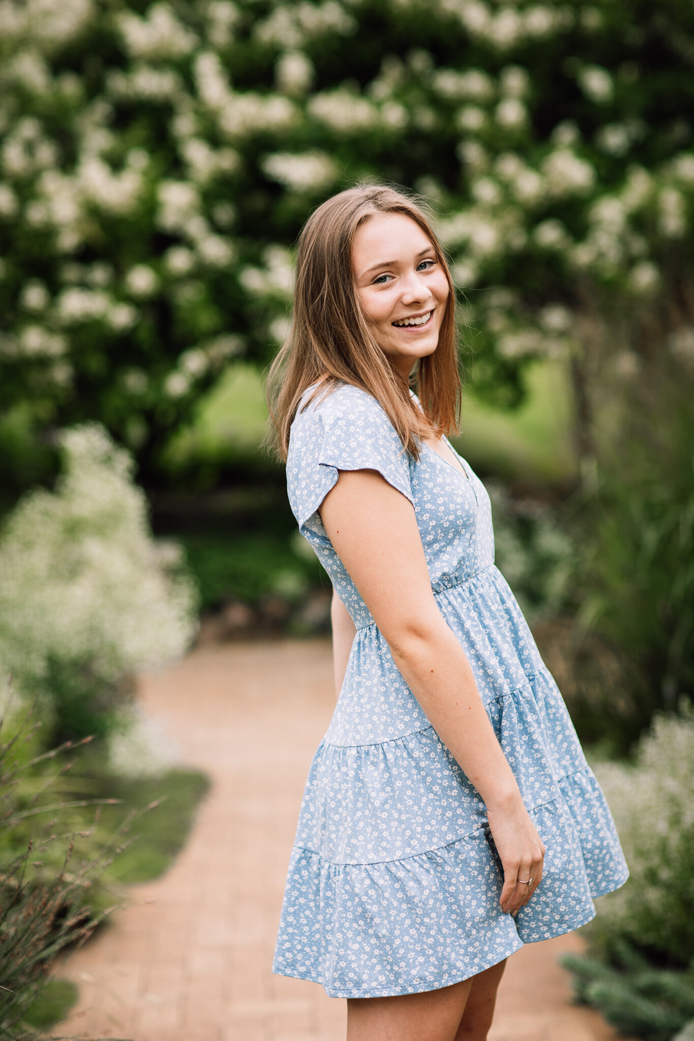 A girl in a blue dress with white flowers is twirling at the Noerenberg Memorial Gardens | Chanhassen Senior Photographer