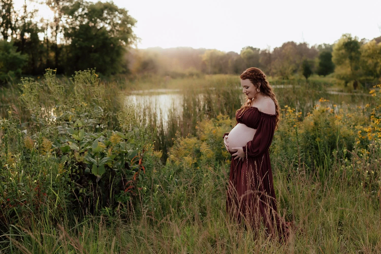 a pregnant woman enjoying her baby bump while standing in a beautiful field at sunset in plymouth, mn