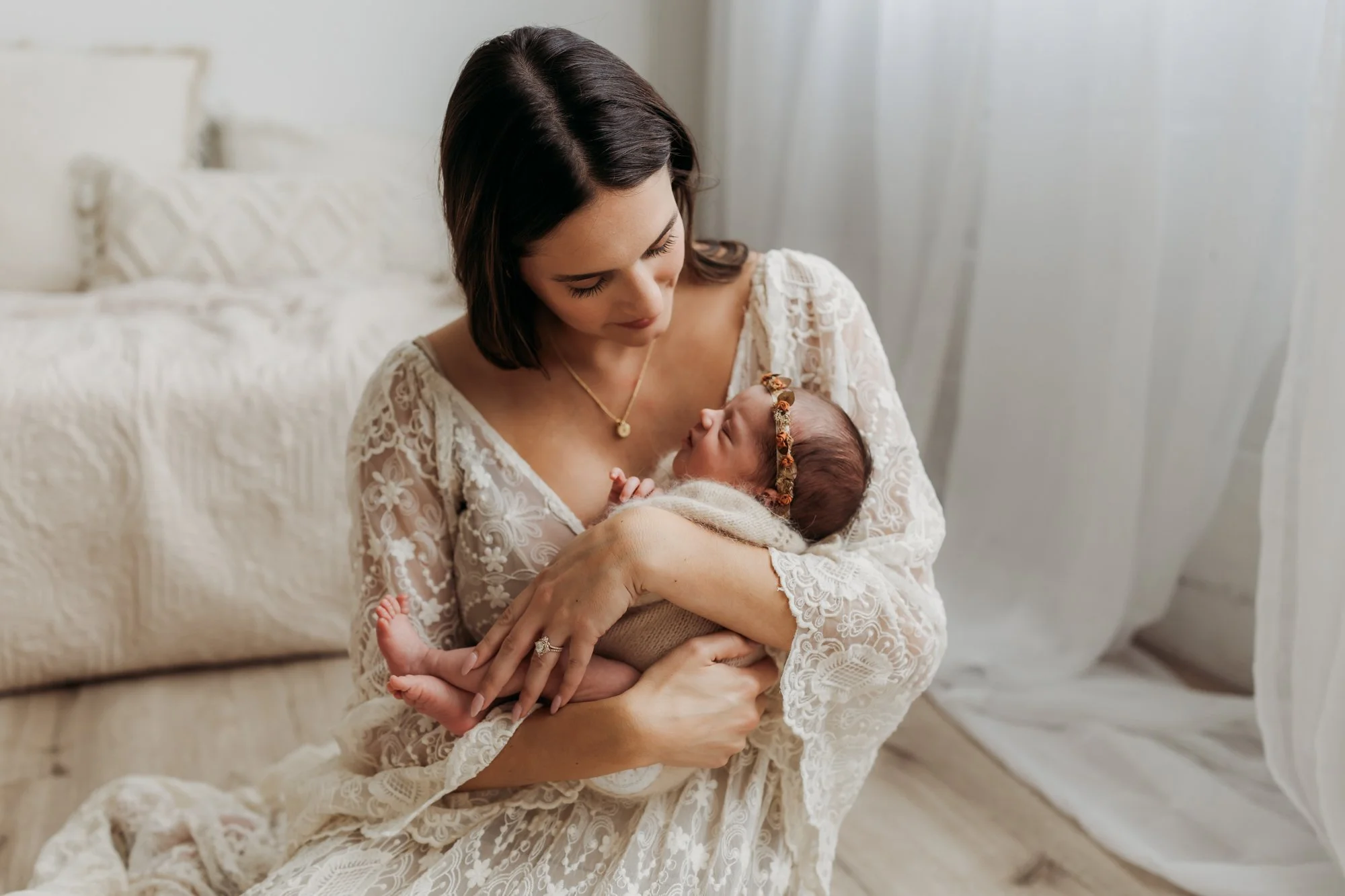 a mom in a lace dress is holding her baby girl during a newborn photo shoot with Ann Marie