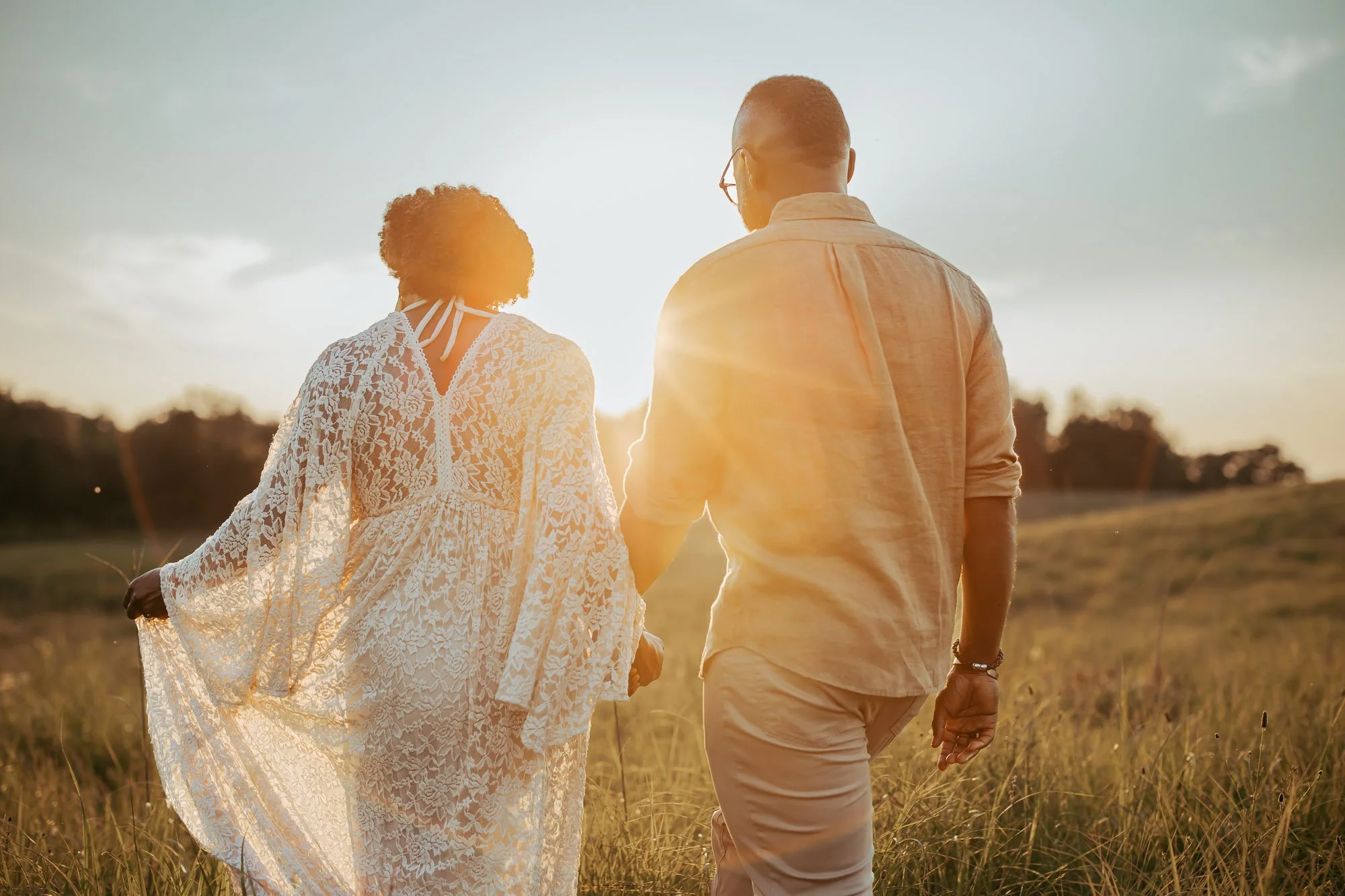 A couple walking hand-in-hand through a grassy field during sunset