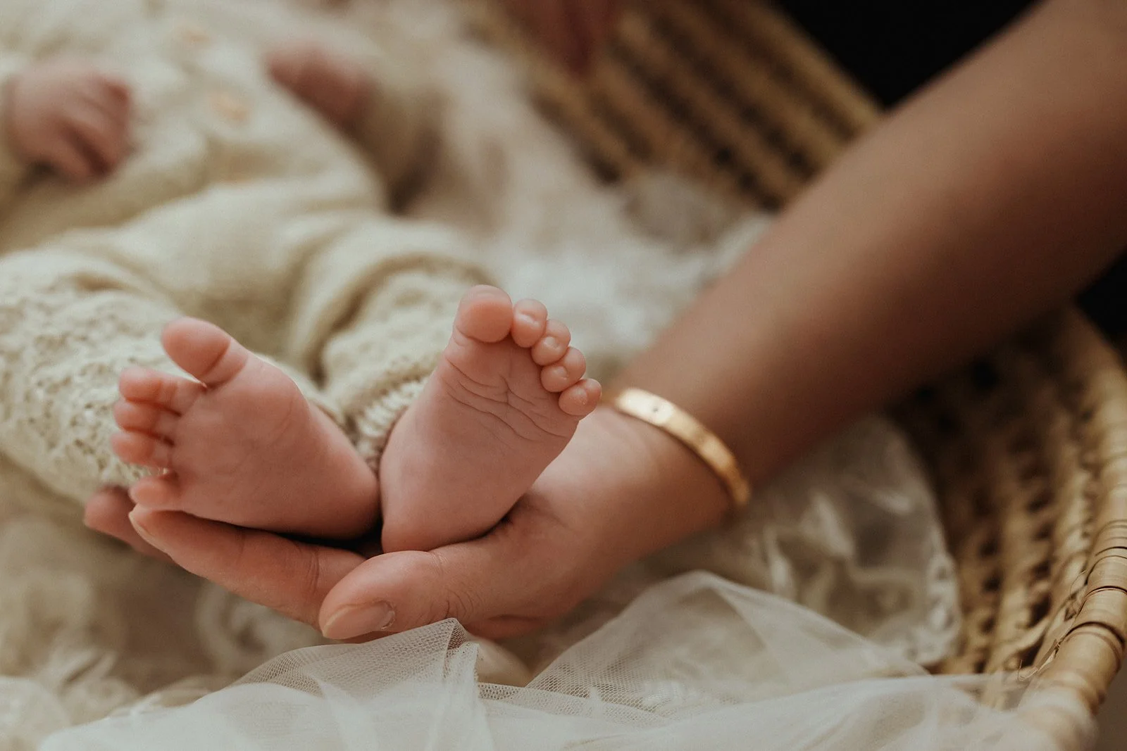 A newborn baby's tiny feet being held by an adult's hand over a soft blanket in a wicker basket.