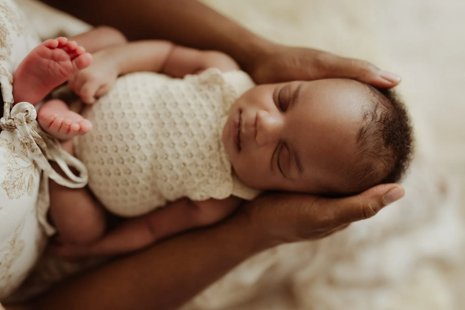 A newborn baby girl wearing a woven jumper sleeps in her mother's arms.