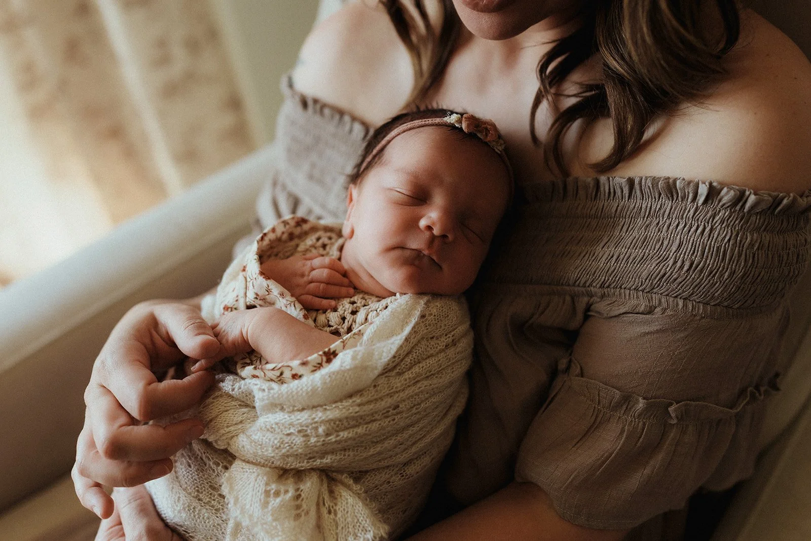 A woman holding a sleeping baby wrapped in a blanket, resting her head against the woman's shoulder.