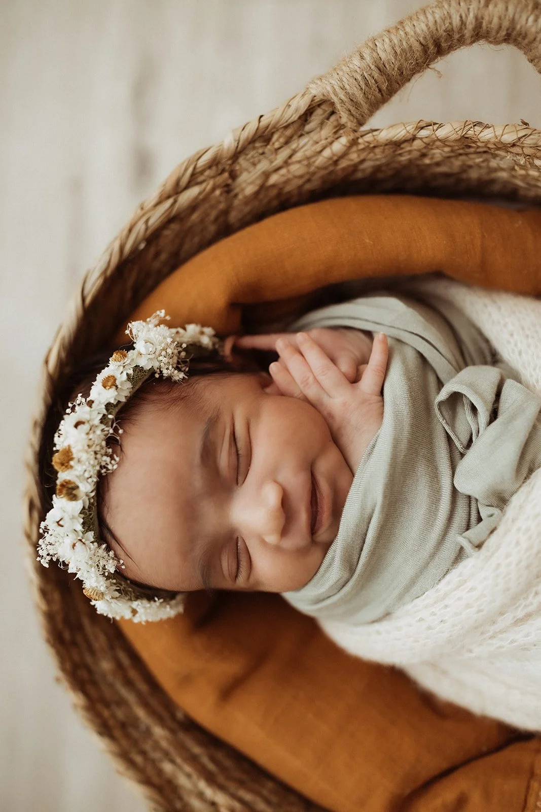 A swaddled, newborn baby smiles in her sleep as she rests in a basket.