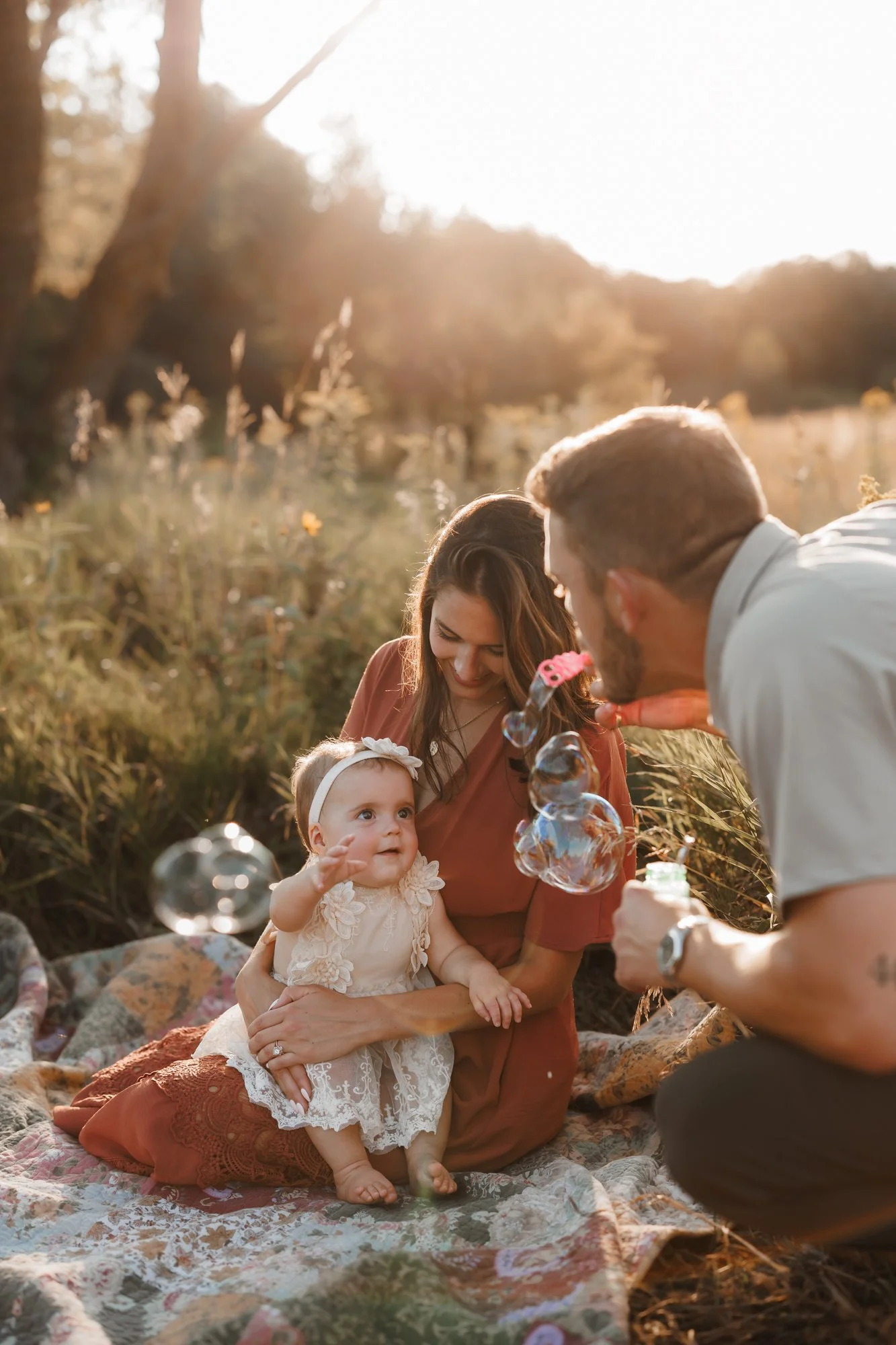 a dad is blowing bubbles with his one year old daughter during family photos
