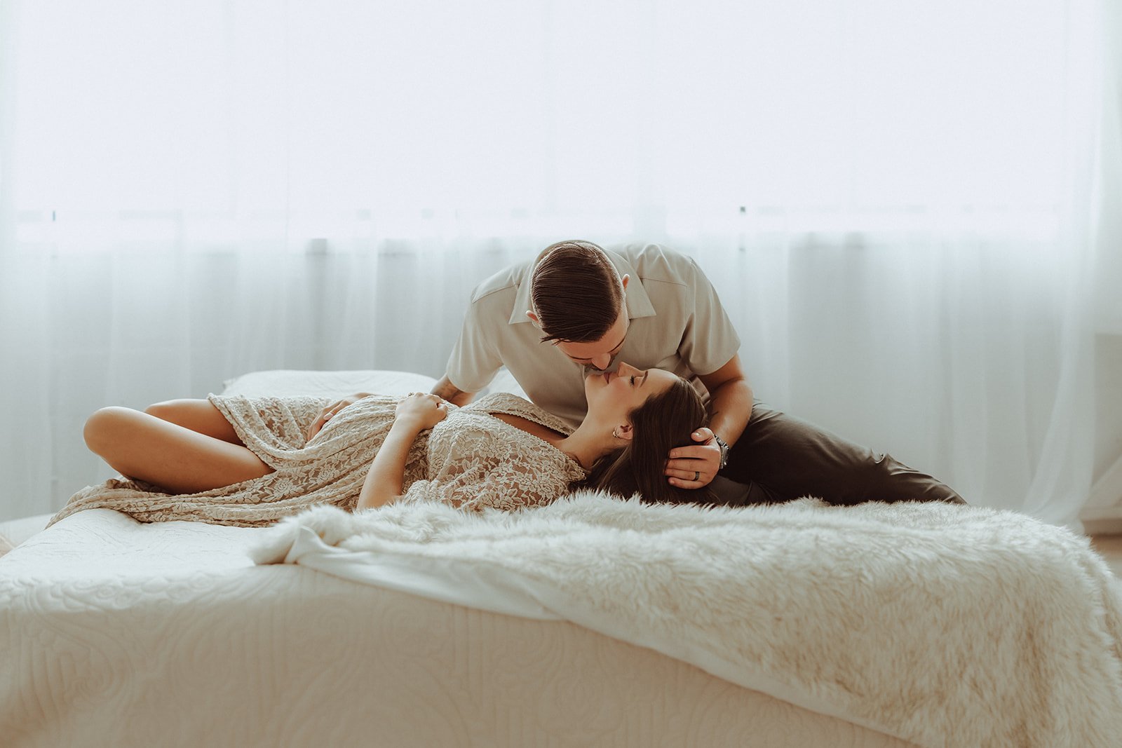 A couple sharing a close, intimate moment on a bed in a softly lit room.