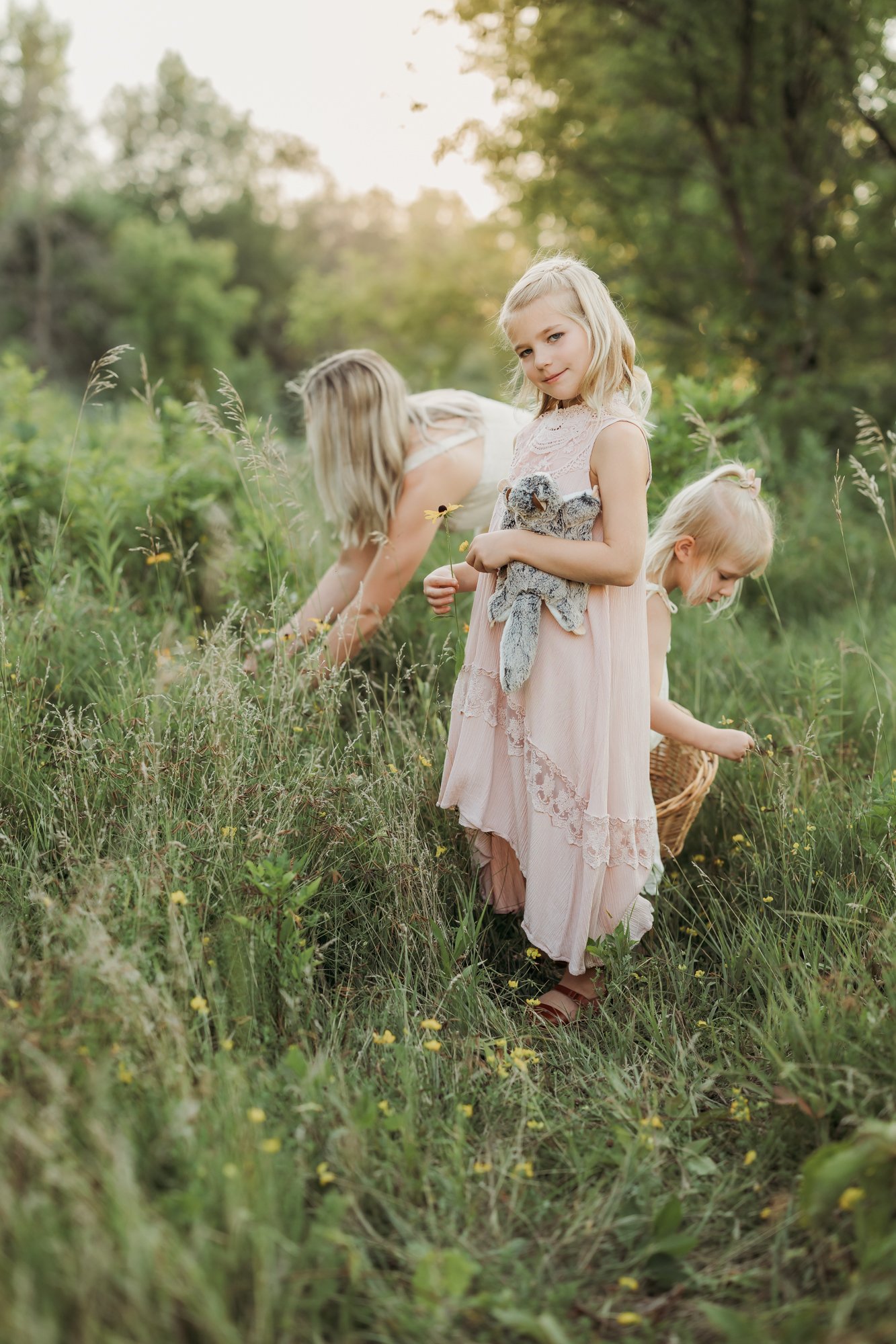 a mom and her two daughters are picking wildflowers at Elm Creek Park Reserve in Maple Grove, MN during a family photo shoot with AMG Photography