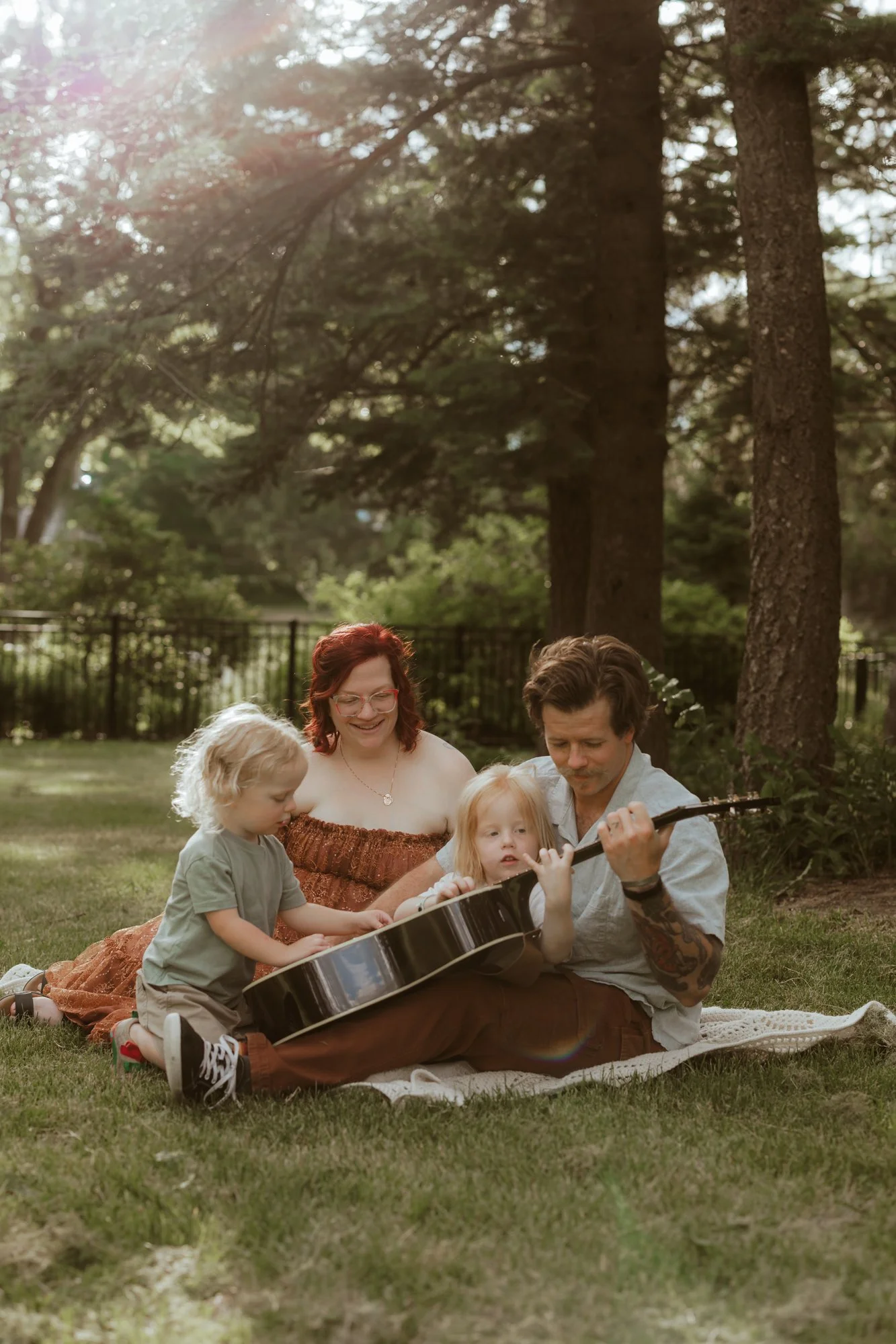 dad is playing guitar for his family during family pictures at Arneson Acres Park in Edina, MN