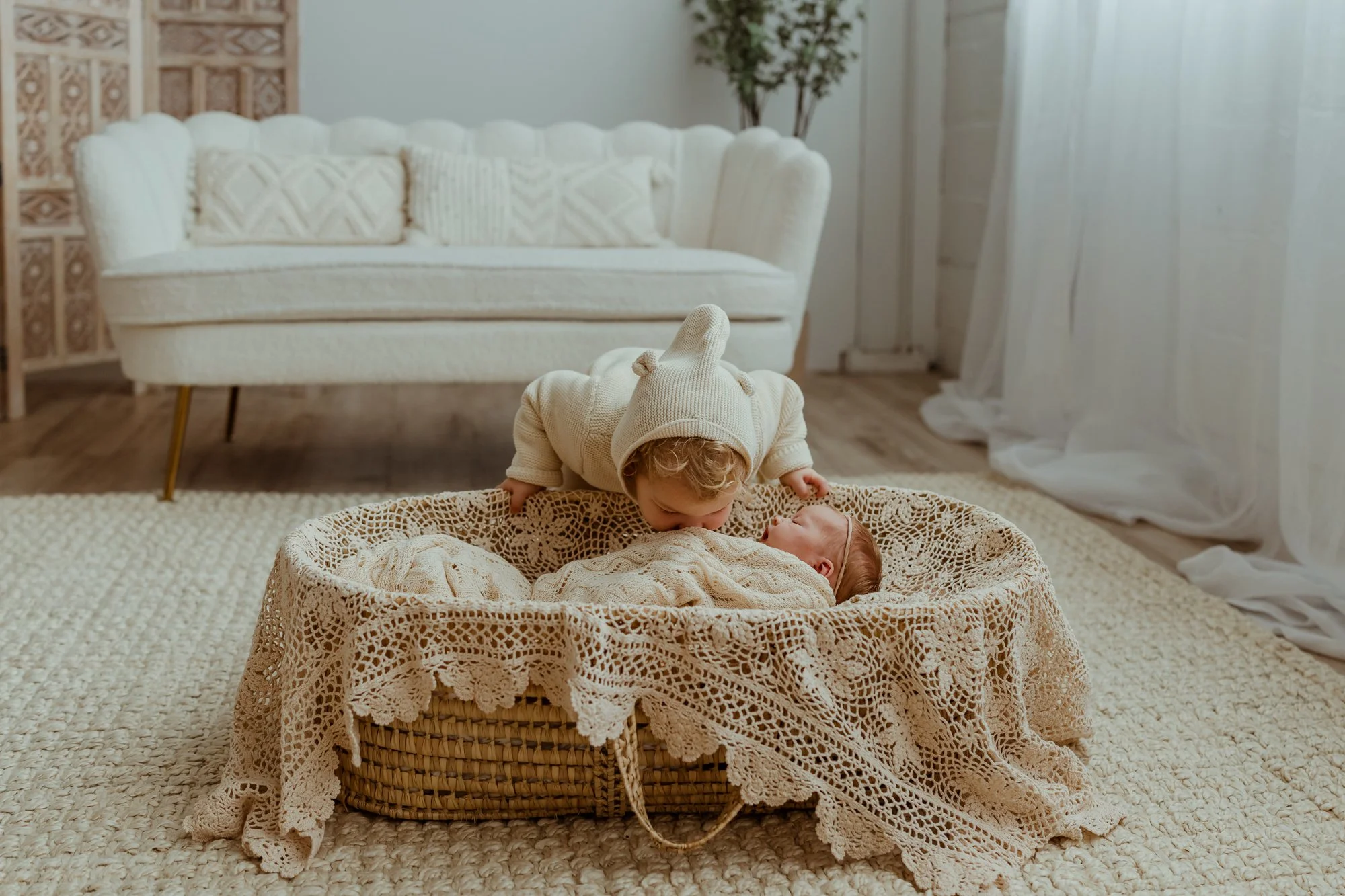 a toddler boy kisses his new baby sister while she sleeps in a bassinet