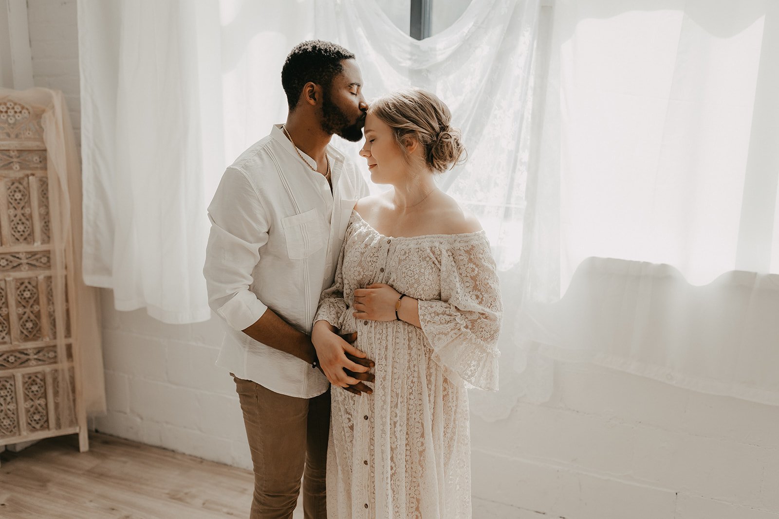 A man kisses his pregnant wife on the forehead.
