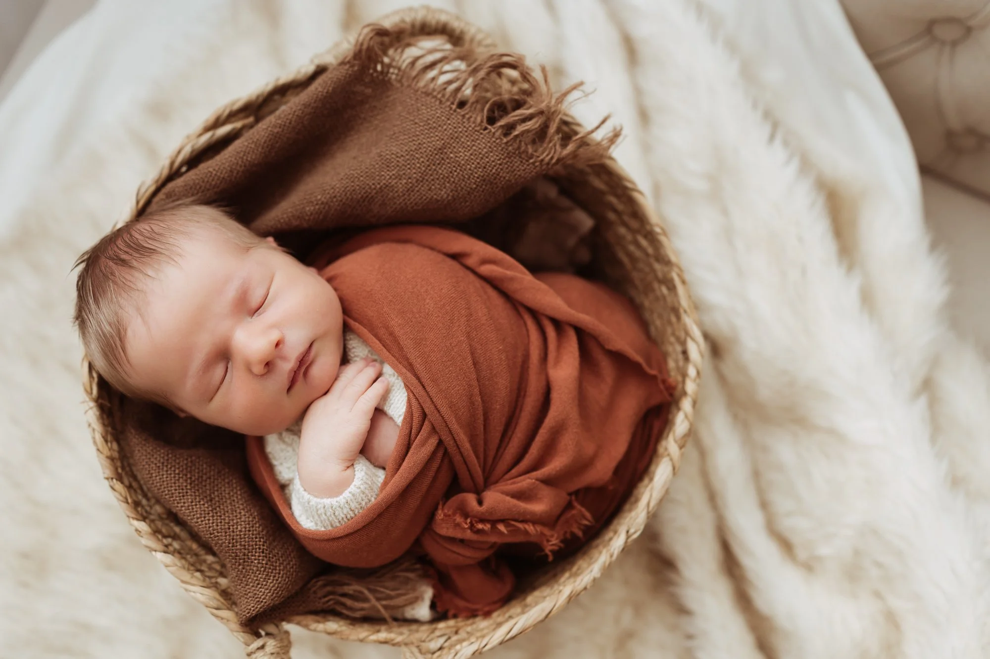 baby boy swaddled in a rust colored blanket is sleeping in a basket