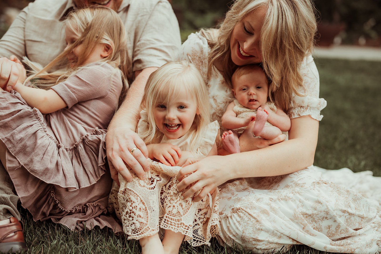 a family of 5 is cuddling on a blanket outside in the summer during a newborn photo shoot in Minnesota with Ann Marie of AMG Photography