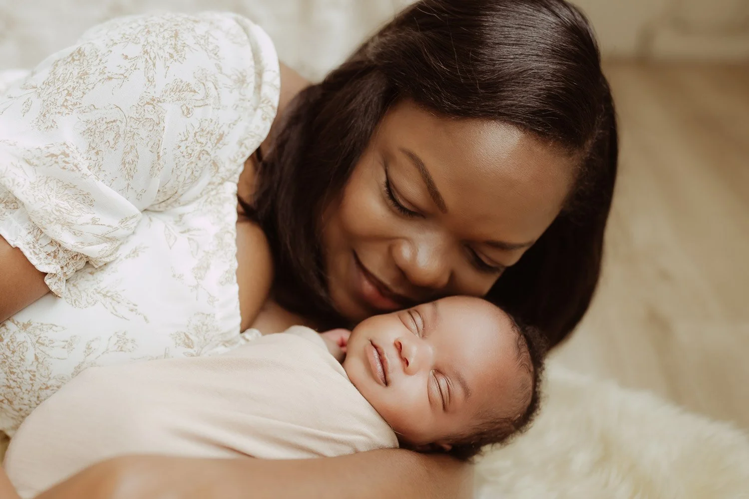 A mother lays on the floor while holding her baby girl.
