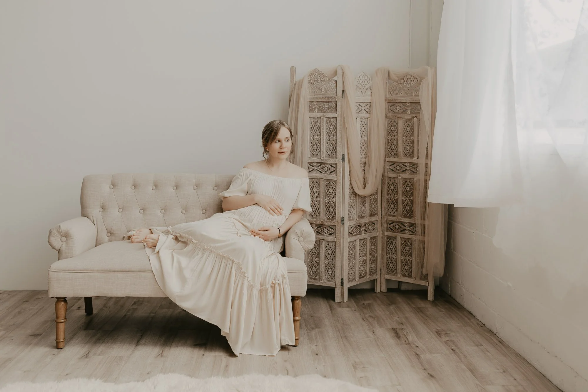 a pregnant woman is reclining on a couch in AMG Photography's studio during her maternity photo session