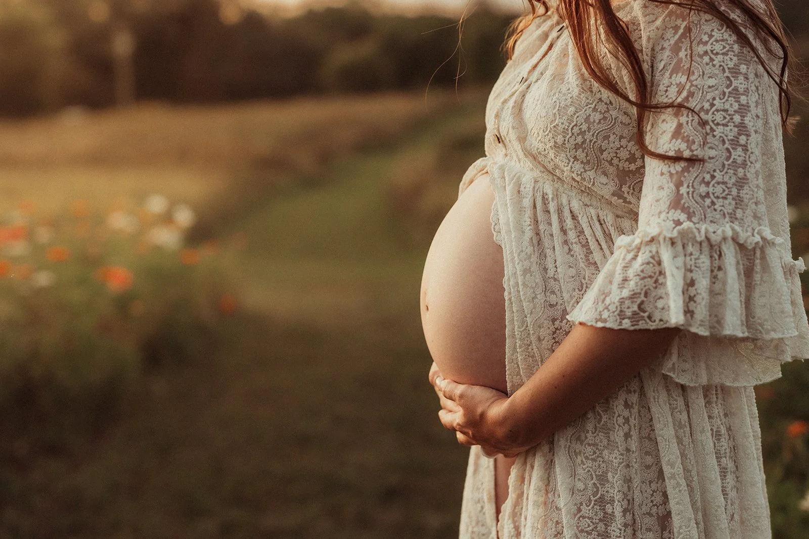 a pregnant woman wearing a lace dress with her baby bump showing for maternity pictures with Ann Marie of AMG Photography