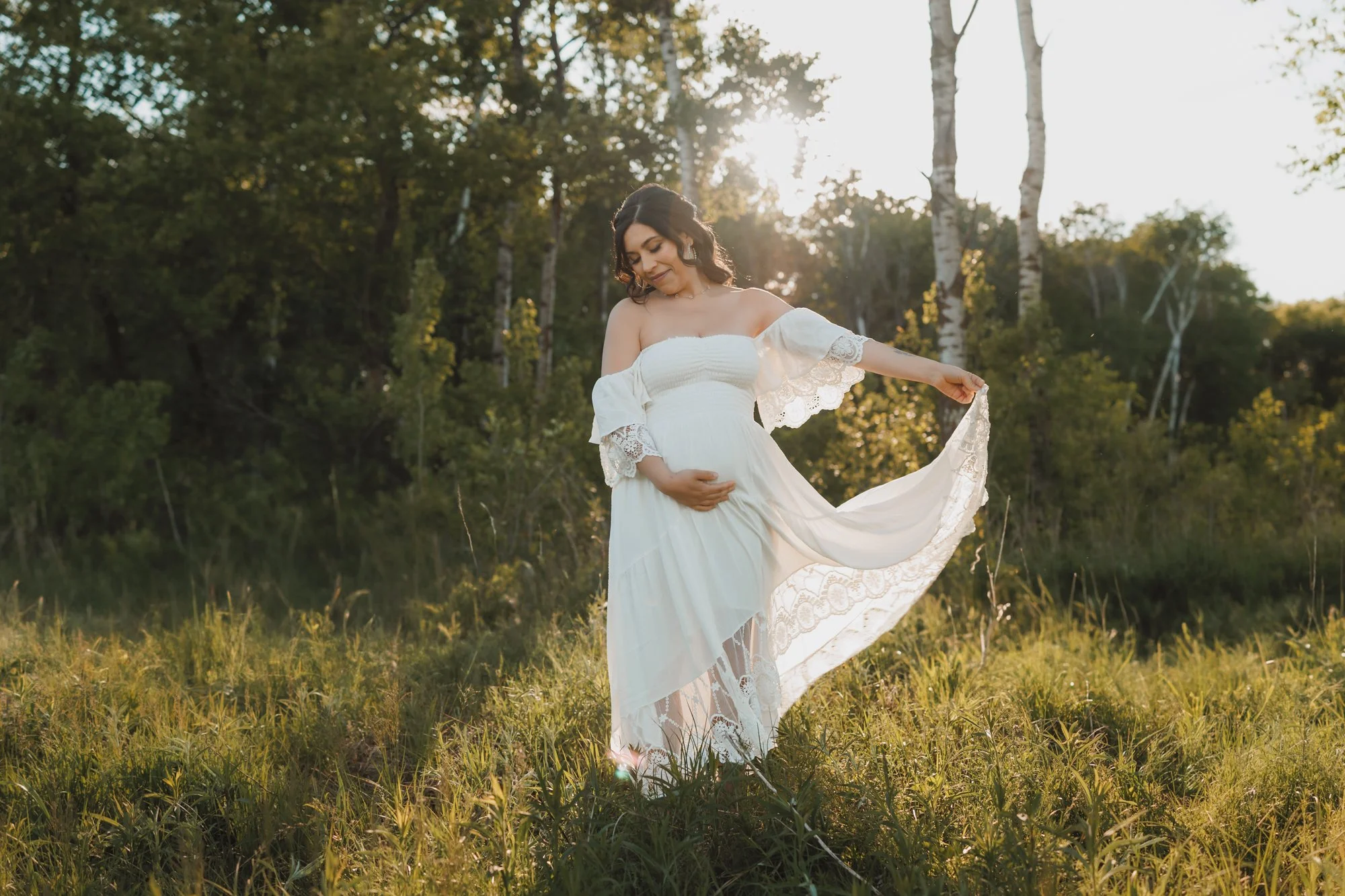 a pregnant woman in a white dress is dancing in the forest at Tamarack Nature Center in White Bear Lake, Minnesota during a maternity photography session with AMG Photography